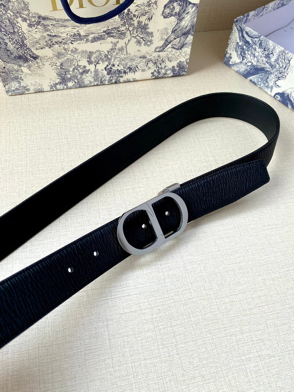 Dior belt close-up showing dark blue textured strap and black buckle plate
