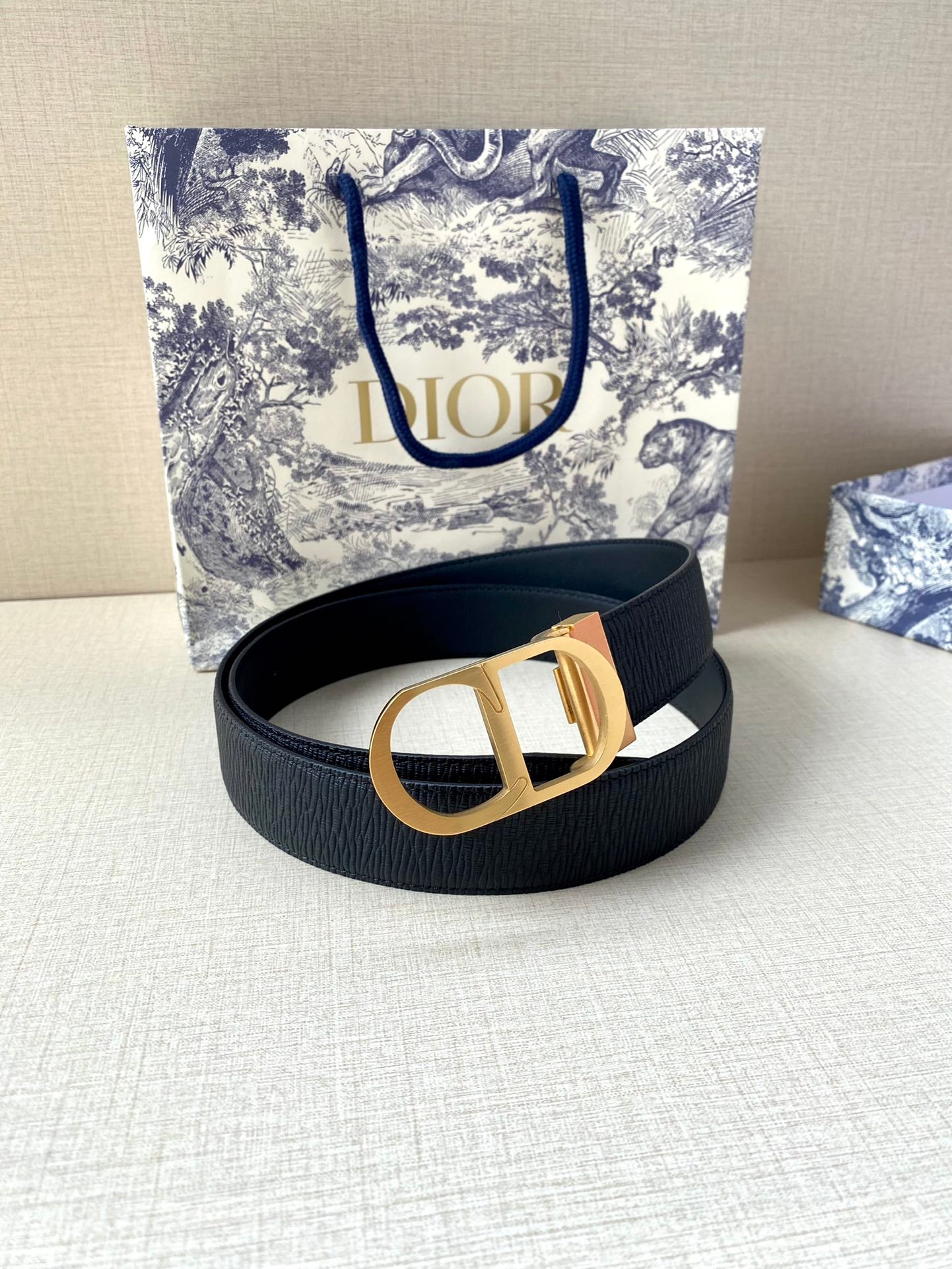Dior belt coiled in dark blue with gold buckle centerpiece on textured strap