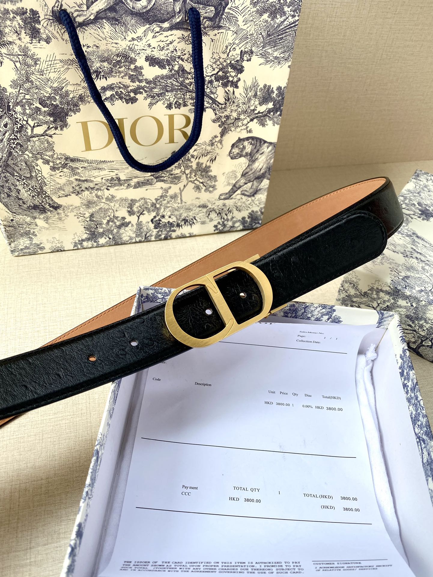 Dior belt with black strap, tan lining, and gold-tone buckle on display