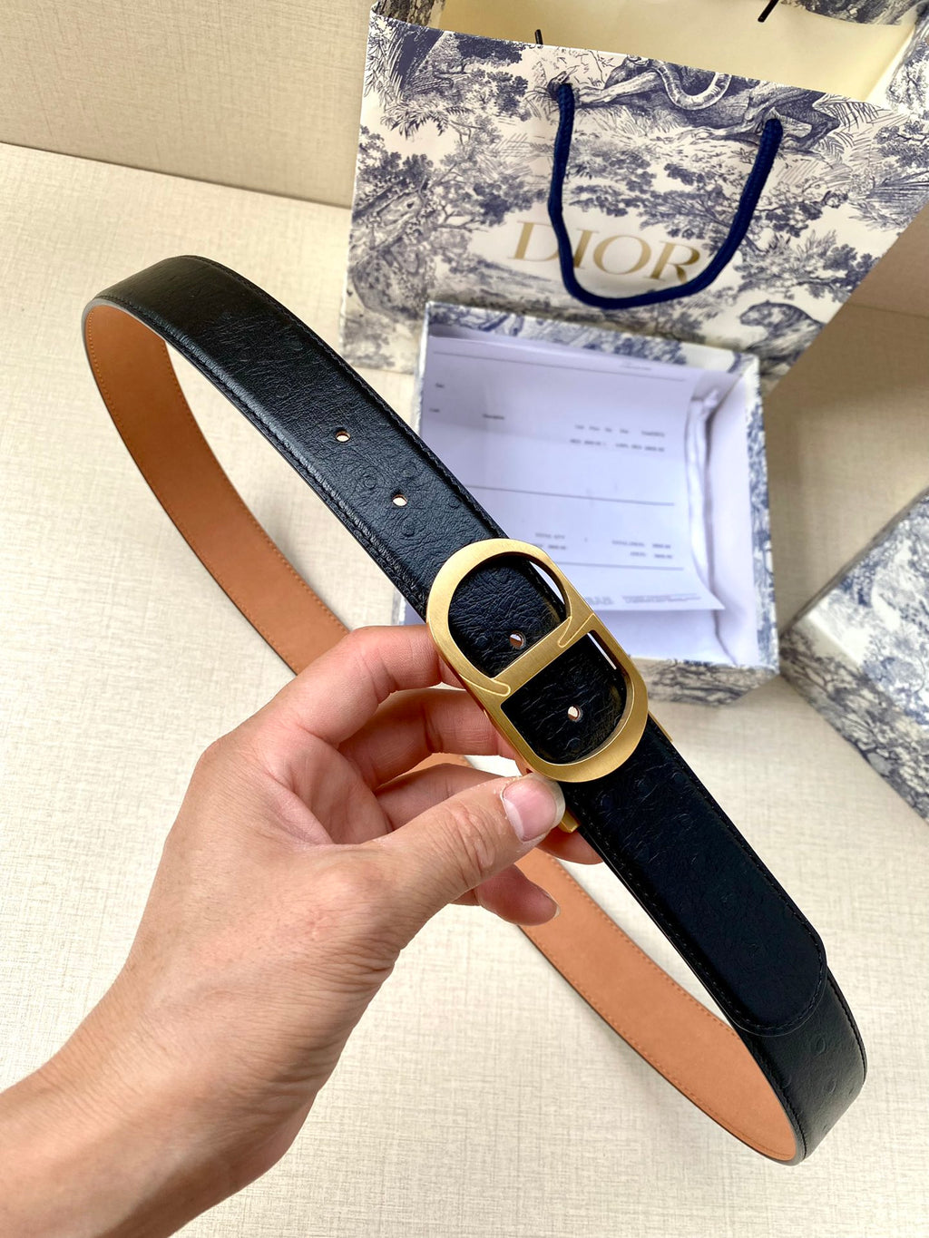 Dior belt with black leather-look strap and gold-tone oval buckle, held in hand