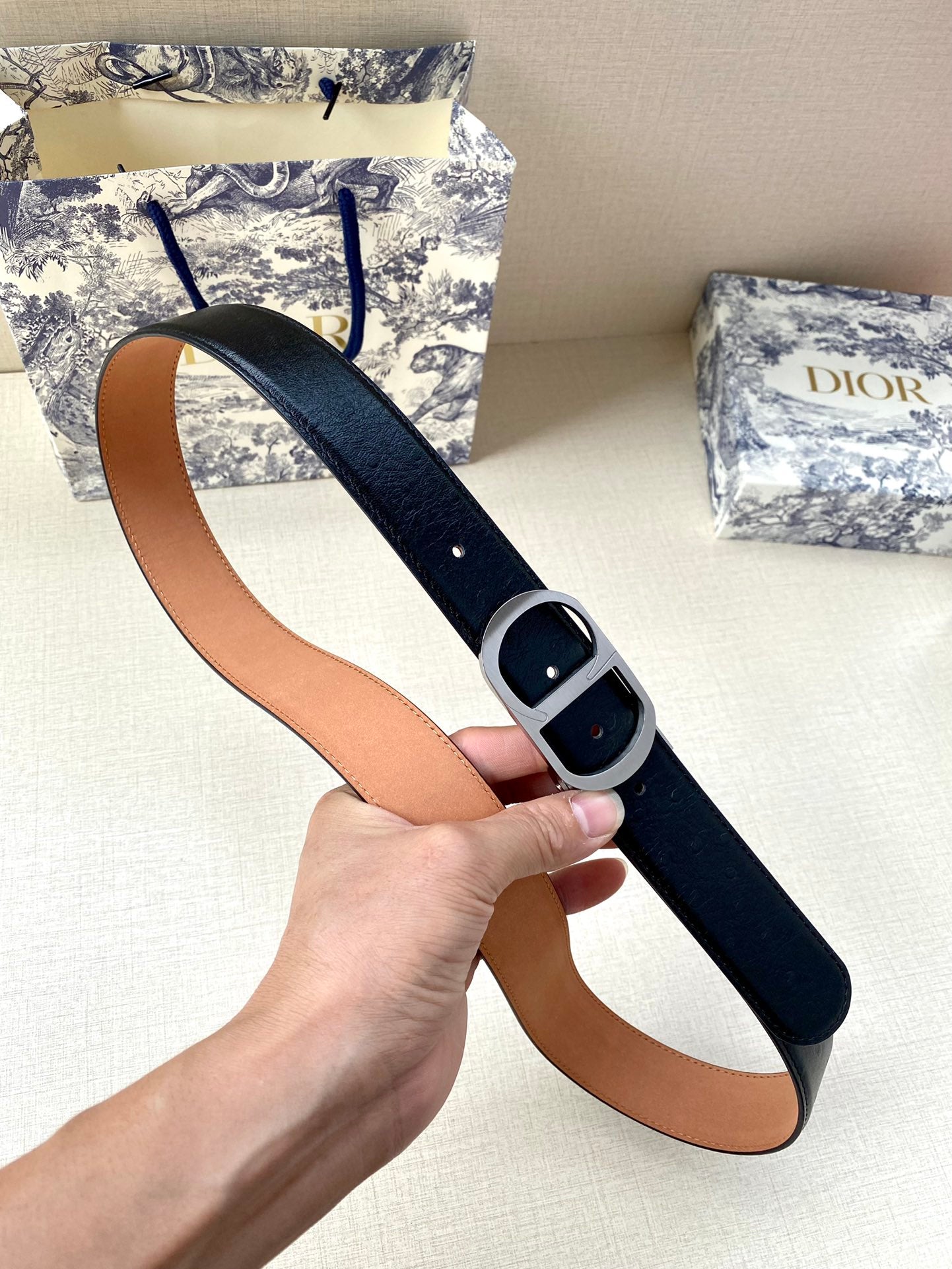 Dior belt held up: black leather-look strap with tan lining and dark buckle
