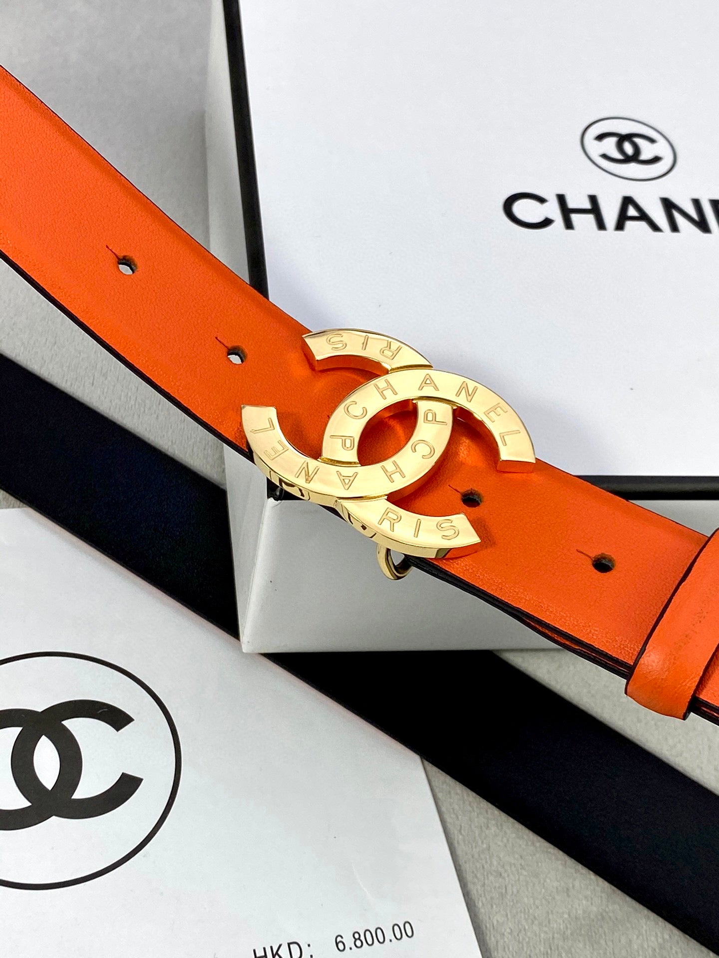 Close view of orange belt with gold Chanel CC buckle and black strap edge