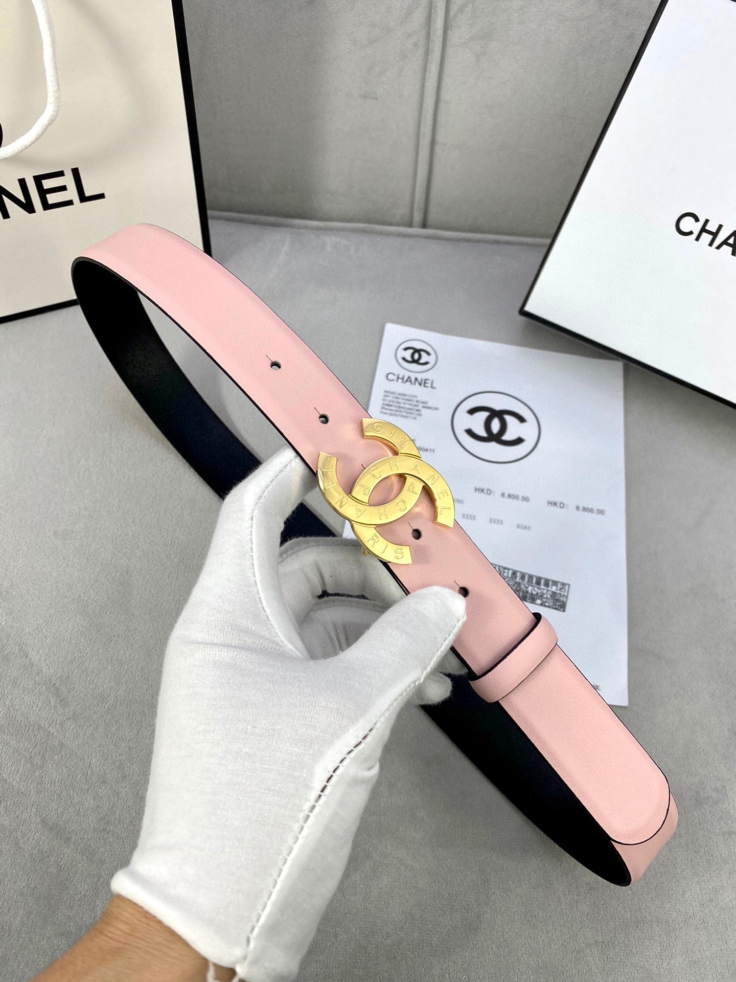 Pink leather belt with gold-tone Chanel logo buckle held by white glove.