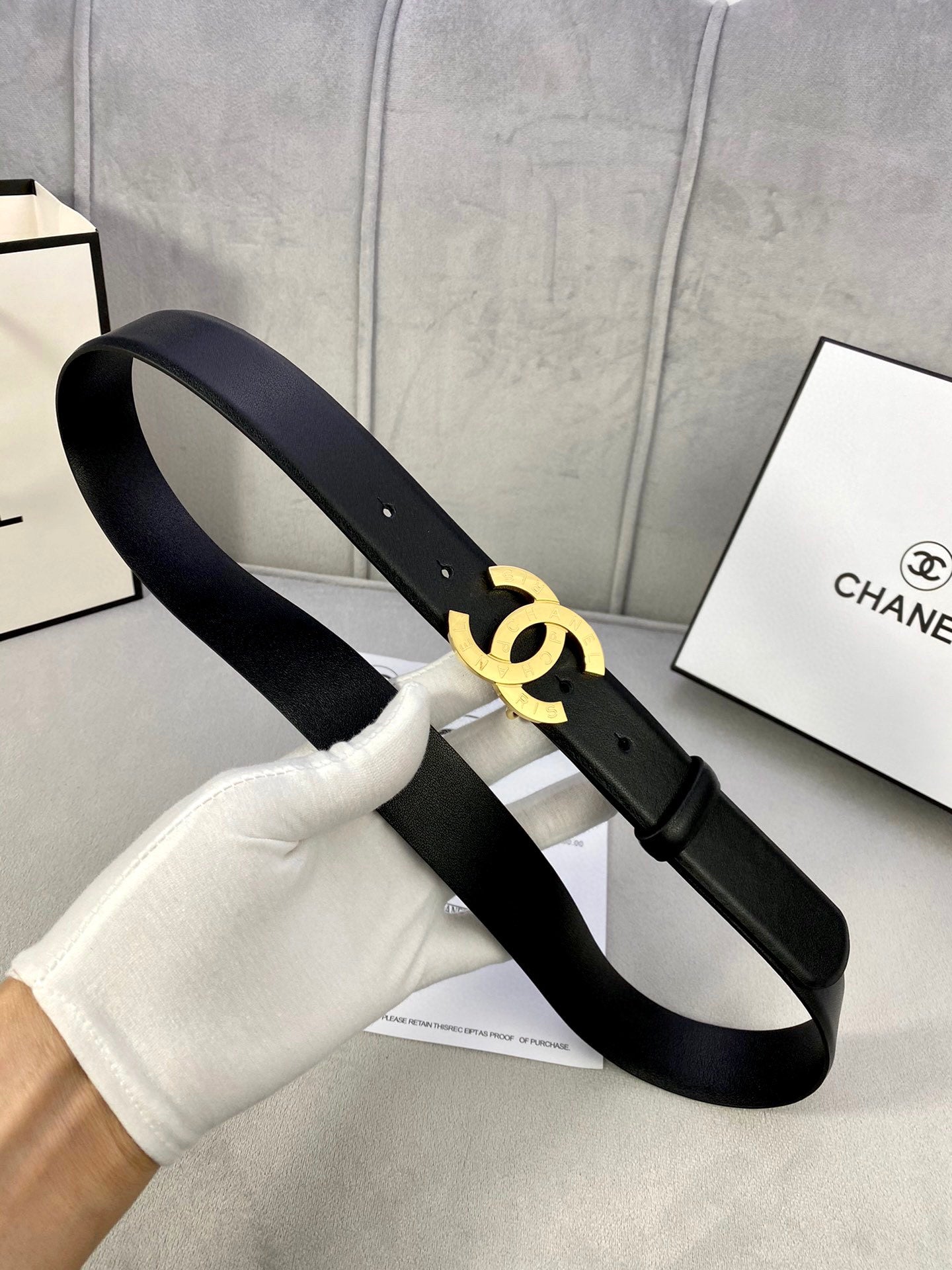 Dark navy leather belt with gold CC buckle, held in white glove