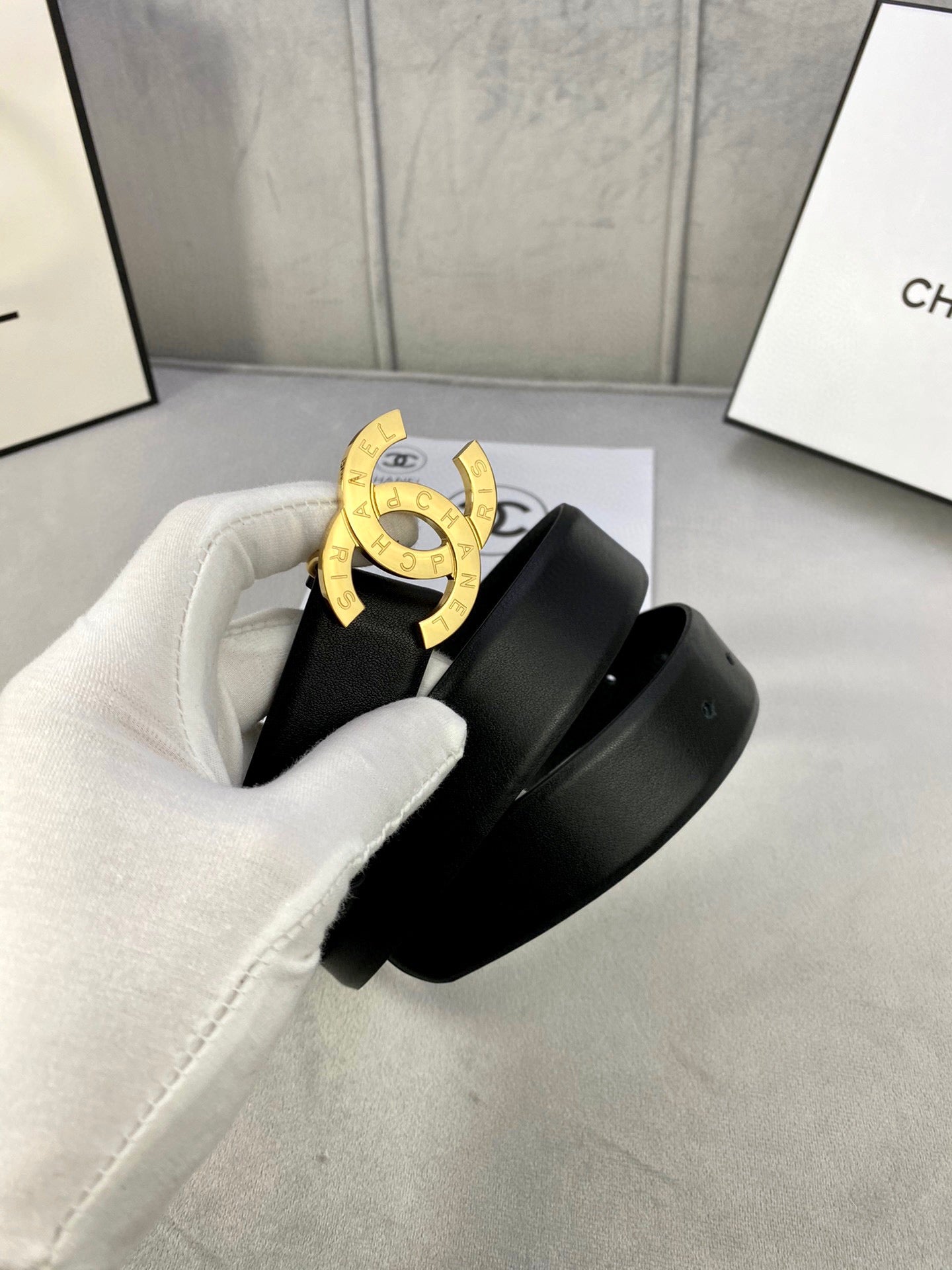 Black leather belt with gold CC buckle, held in white glove