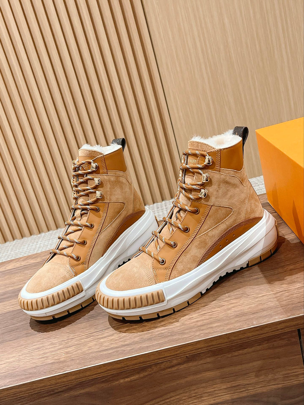 Tan suede Louis Vuitton high-top sneakers with gold-tone eyelets, white soles, and laces