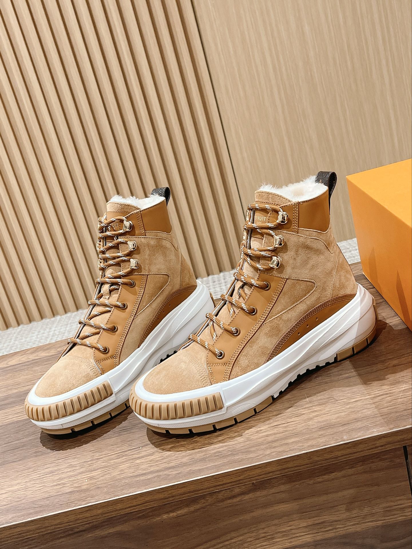 Tan suede Louis Vuitton high-top sneakers with gold-tone eyelets, white soles, and laces