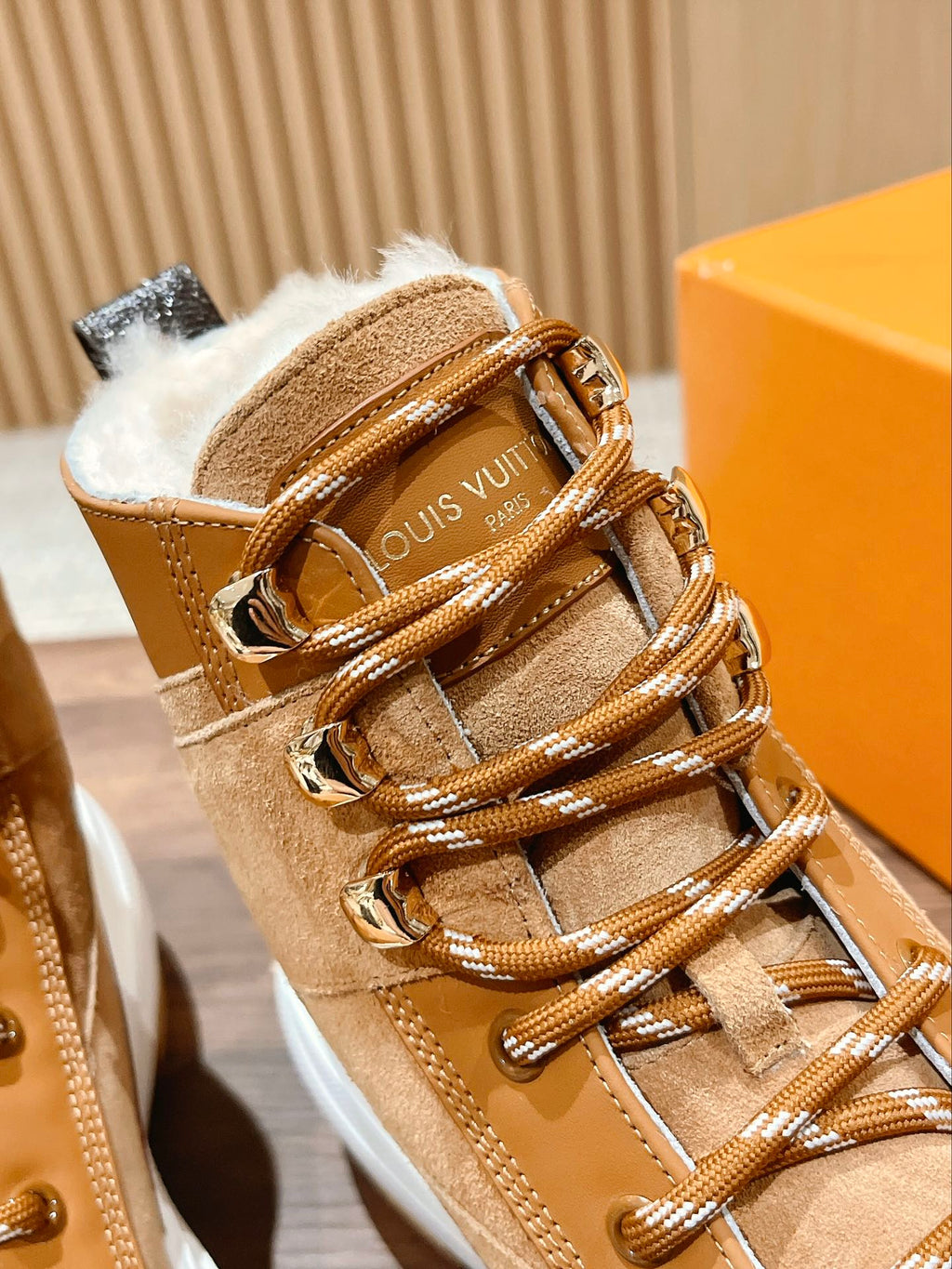 Close-up of tan Louis Vuitton high-top sneaker with fur lining, laces, and gold hardware