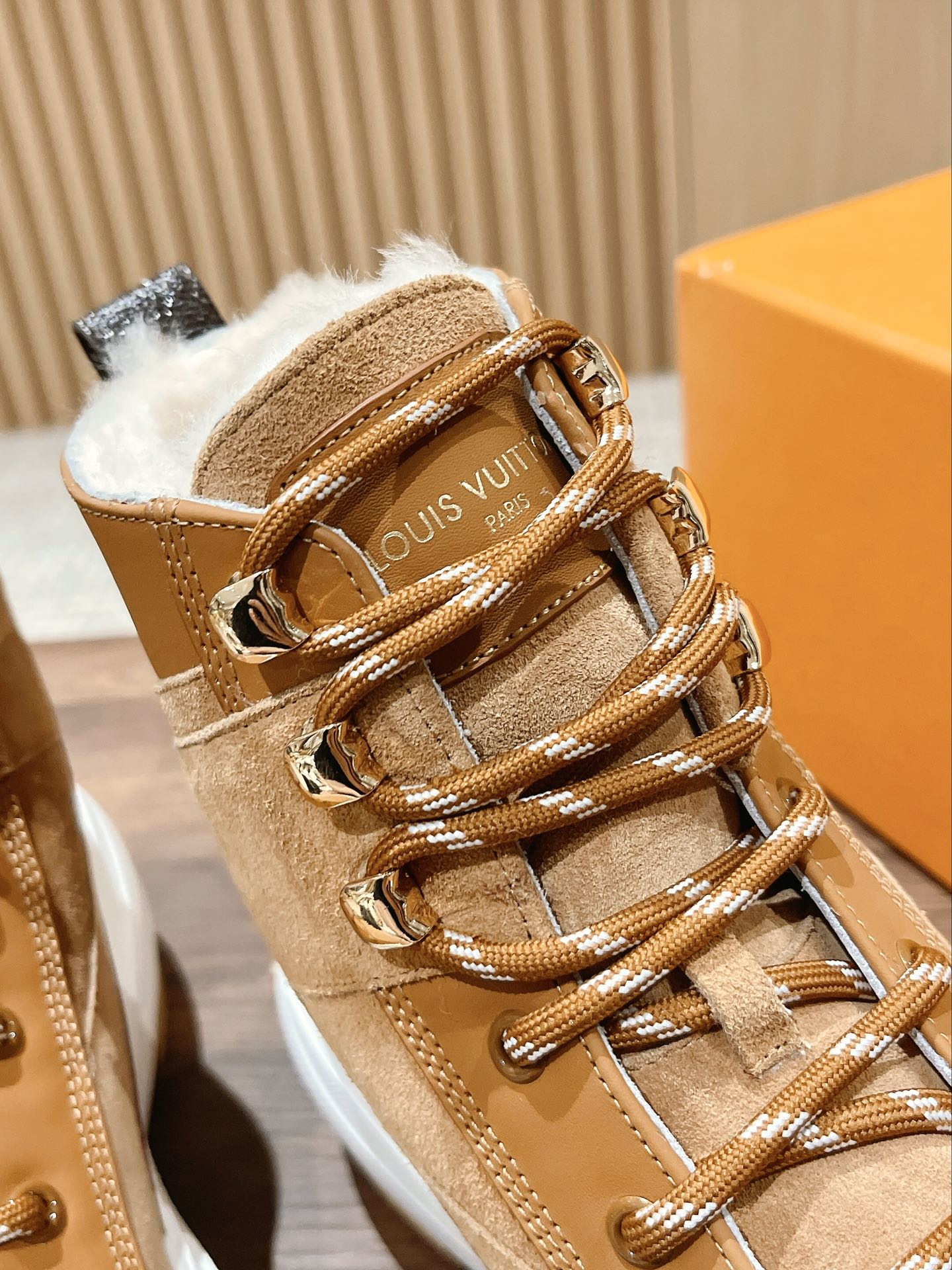 Close-up of tan Louis Vuitton high-top sneaker with fur lining, laces, and gold hardware
