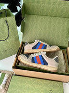Cream low-top sneakers in open box with blue side stripe and multicolor accents.