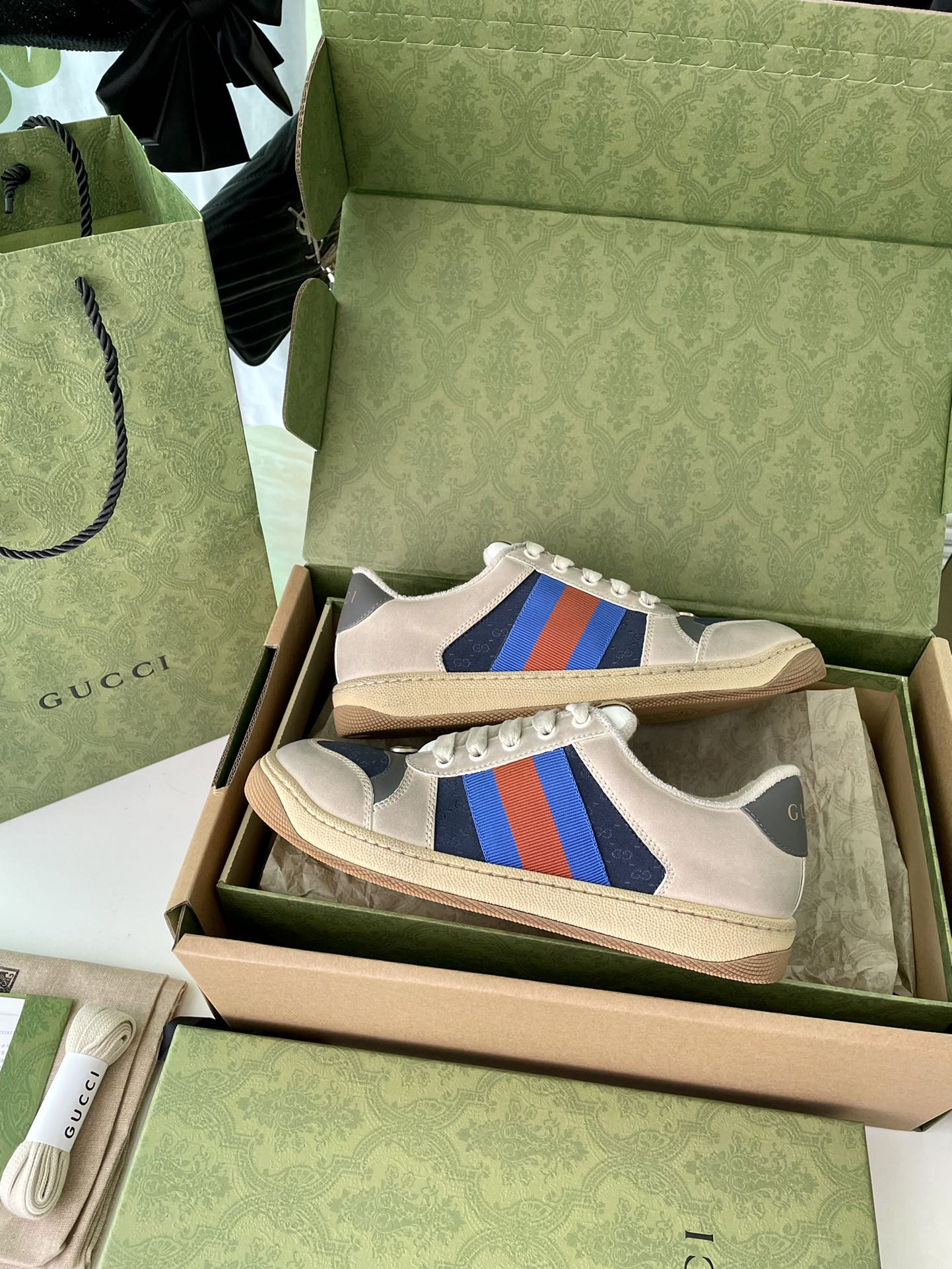Cream low-top sneakers in open box with blue side stripe and multicolor accents.