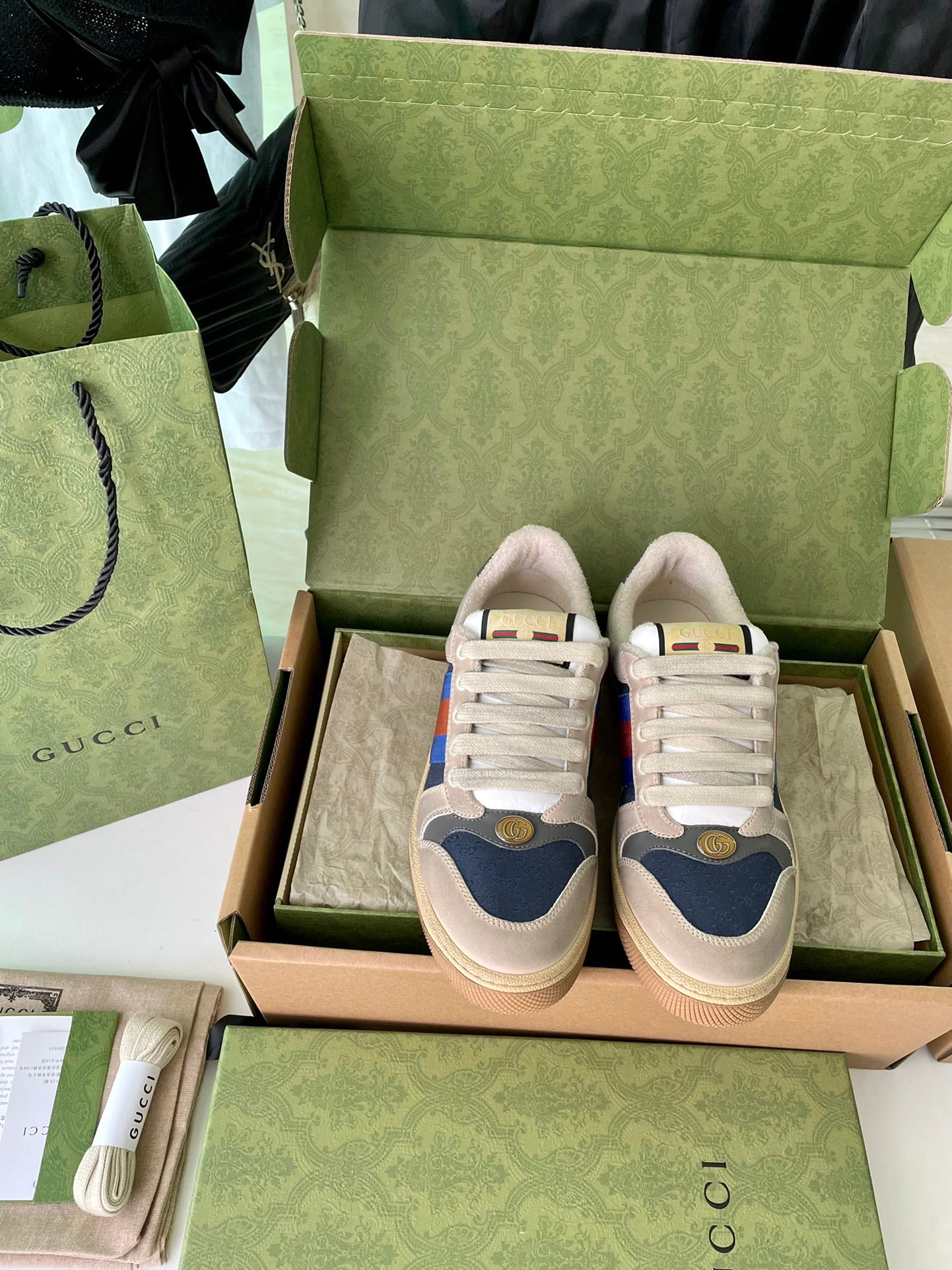 Cream sneakers in box with multicolor stripe, blue heel patch, and lace-up fronts.