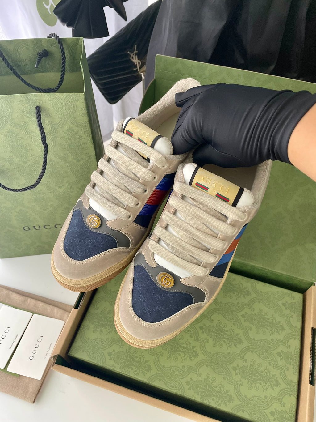 Pair of cream sneakers in box, blue side panels with multicolor stripe and gold logos.