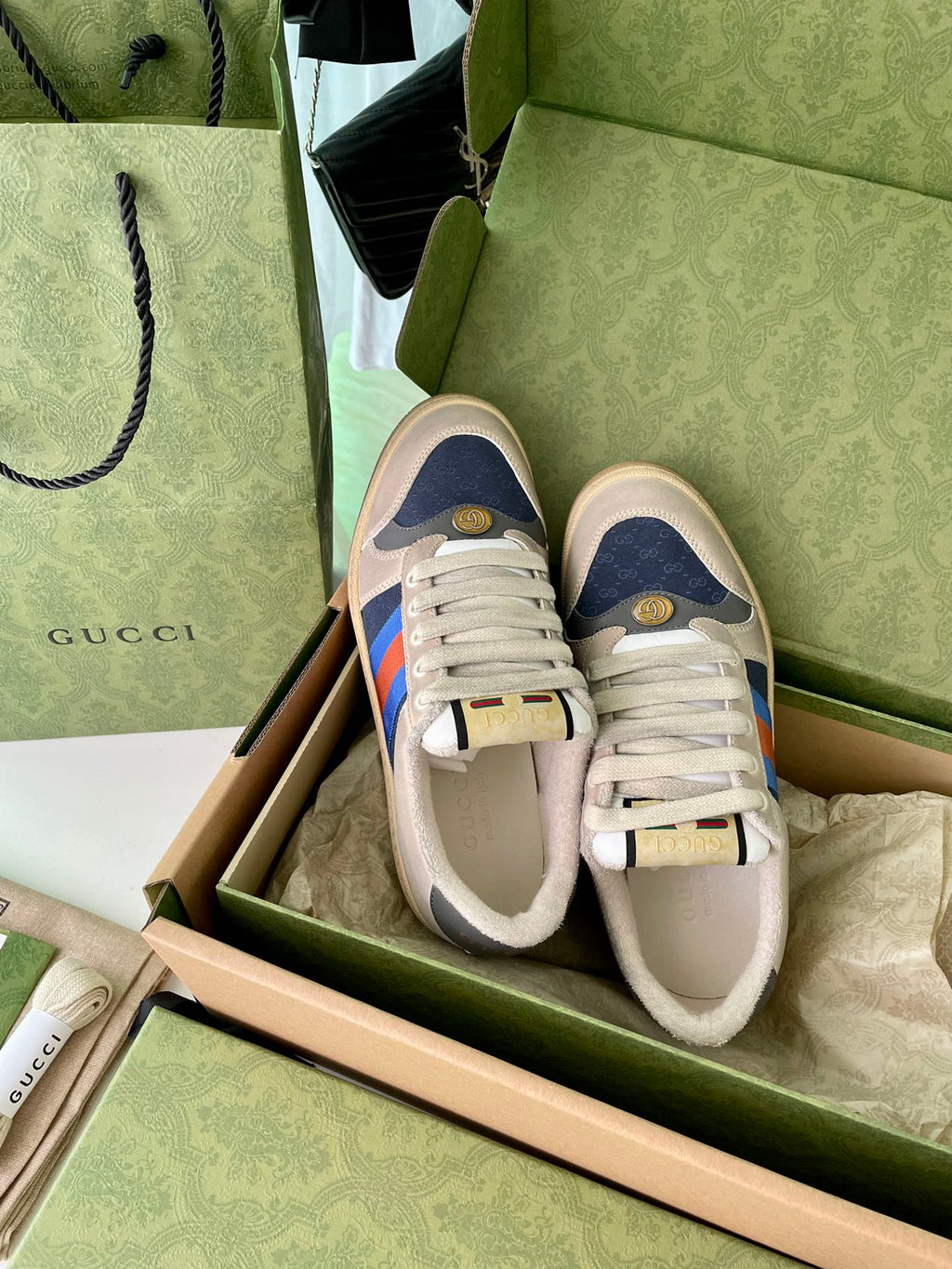 Cream lace-up sneakers in box with multicolor side stripe and blue toe guard.