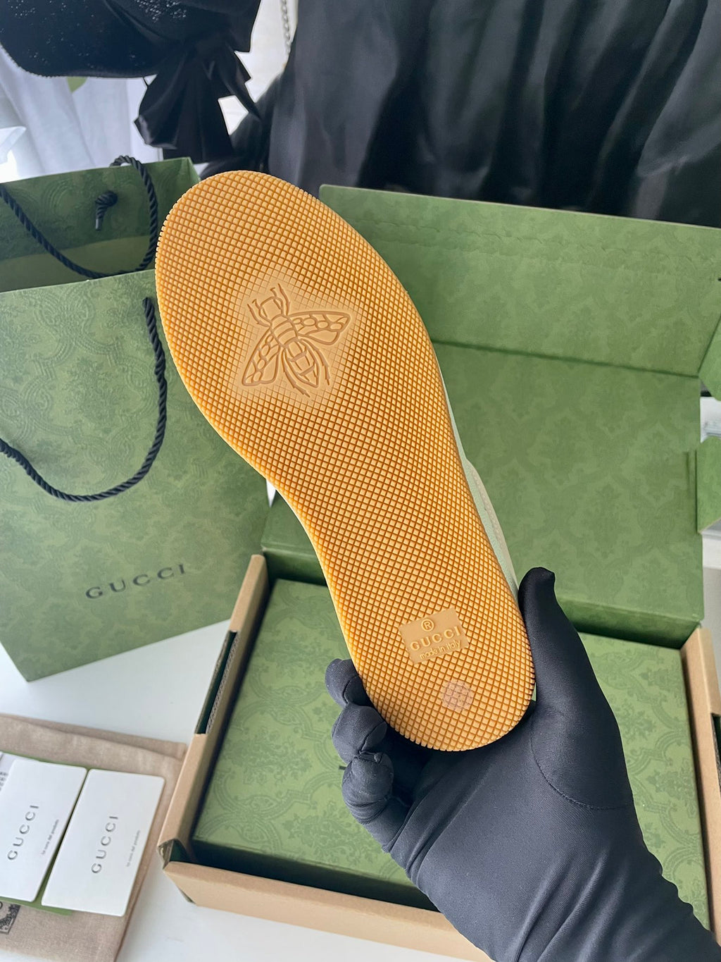 Beige sneaker sole with embossed GUCCI mark, held above green box