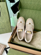 Two beige lace-up sneakers in an open box, featuring side stripe and emblem