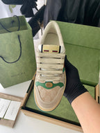Beige Gucci low-top sneakers with lace-up front and green red Web stripe heel tab.