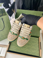 Beige Gucci sneakers with green Web stripe and lace-up front, shown at angle.