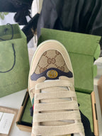 Gucci sneaker toe close-up with beige GG canvas and laces, gold emblem detail.