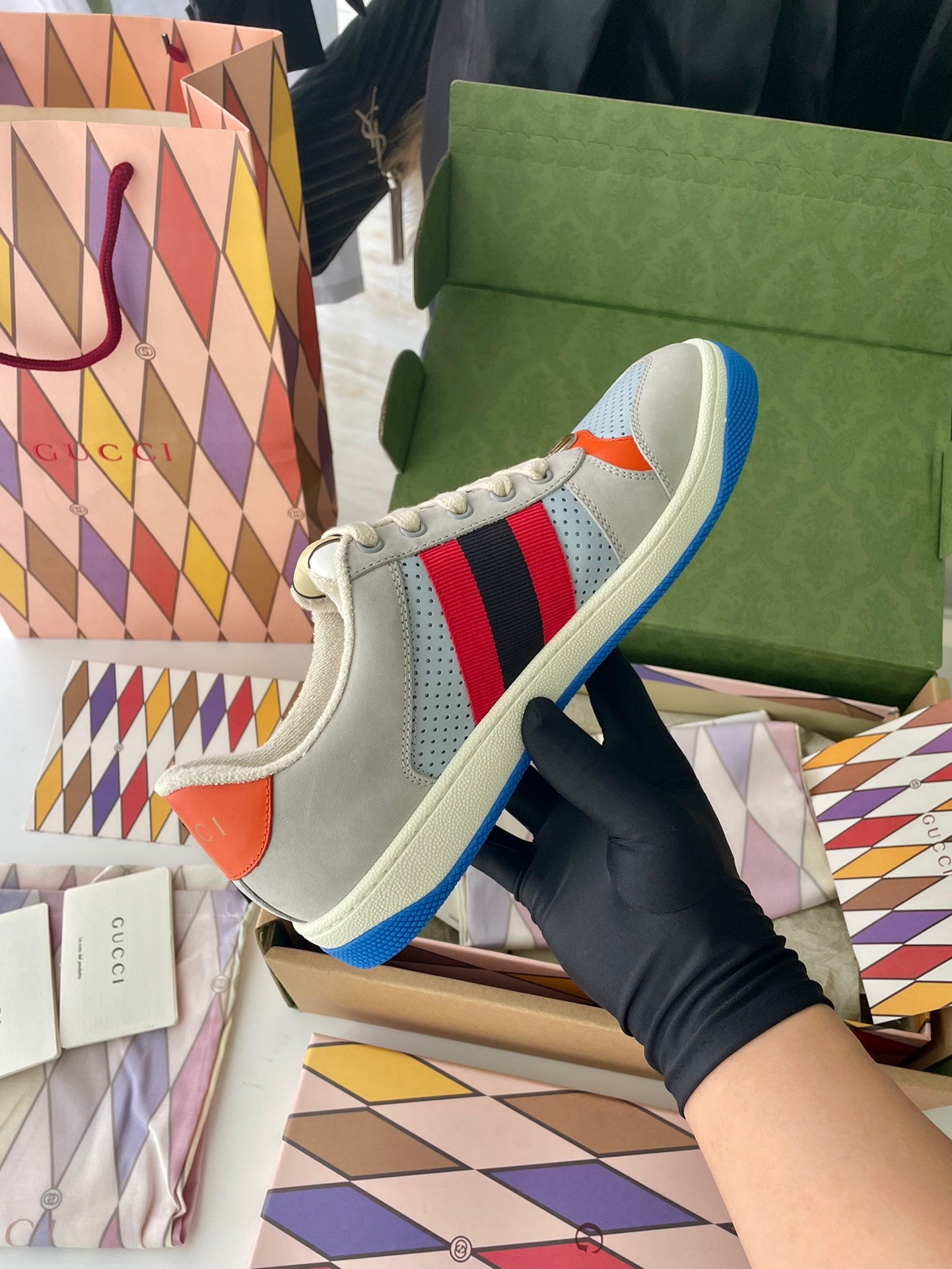 Gucci unisex sneakers front quarter view, light gray with orange side patch and blue sole