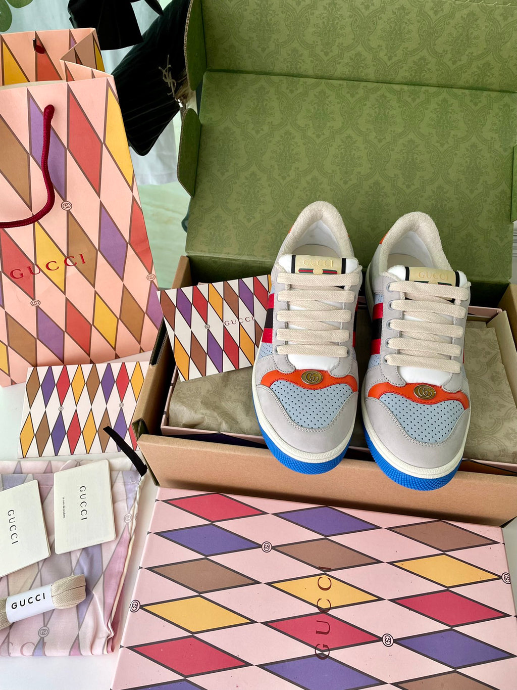 Gucci unisex sneakers pair front view, light gray uppers with orange accents and blue soles