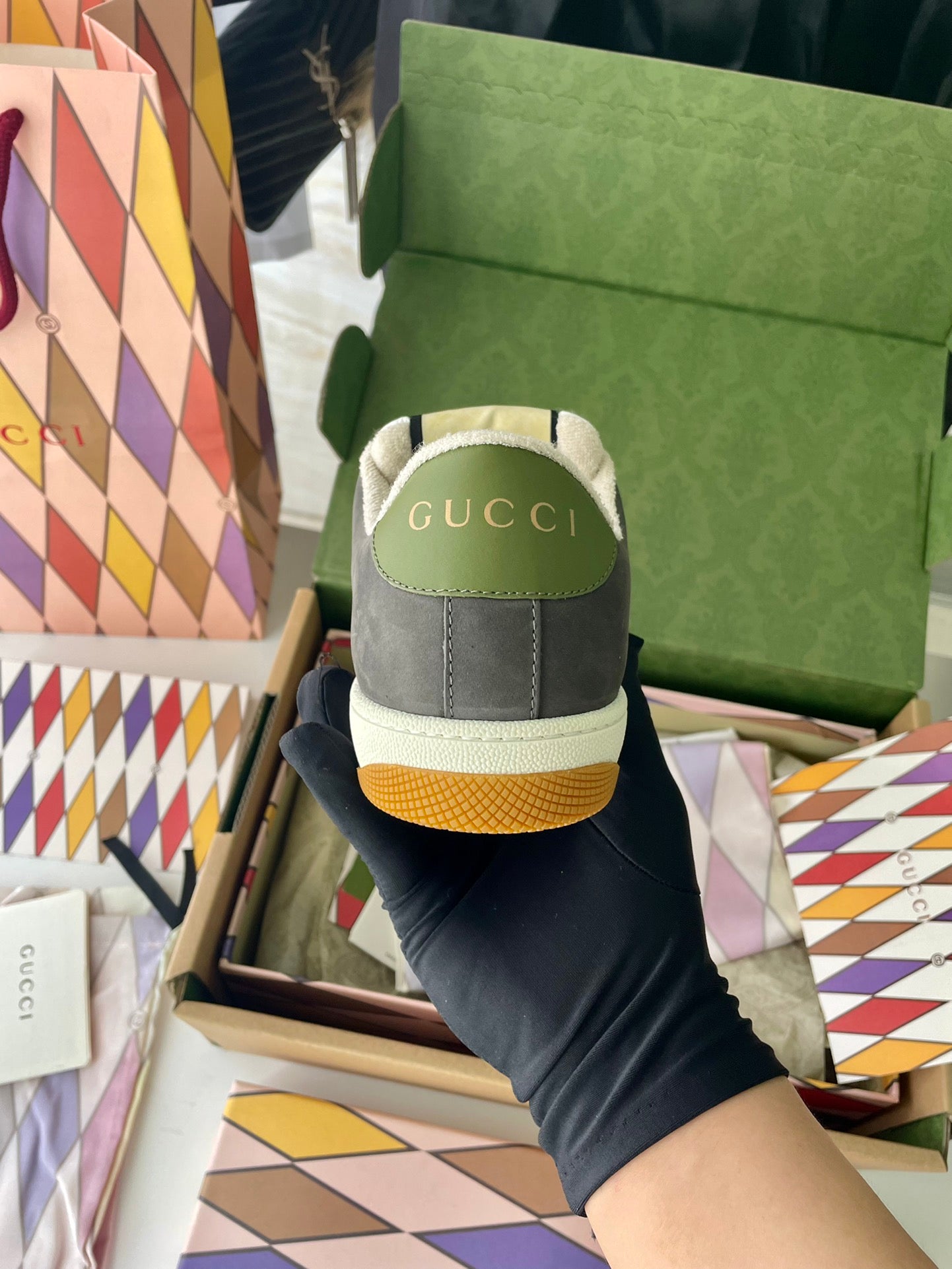 Gucci unisex sneakers heel view with green logo patch, dark gray suede, white rubber sole.