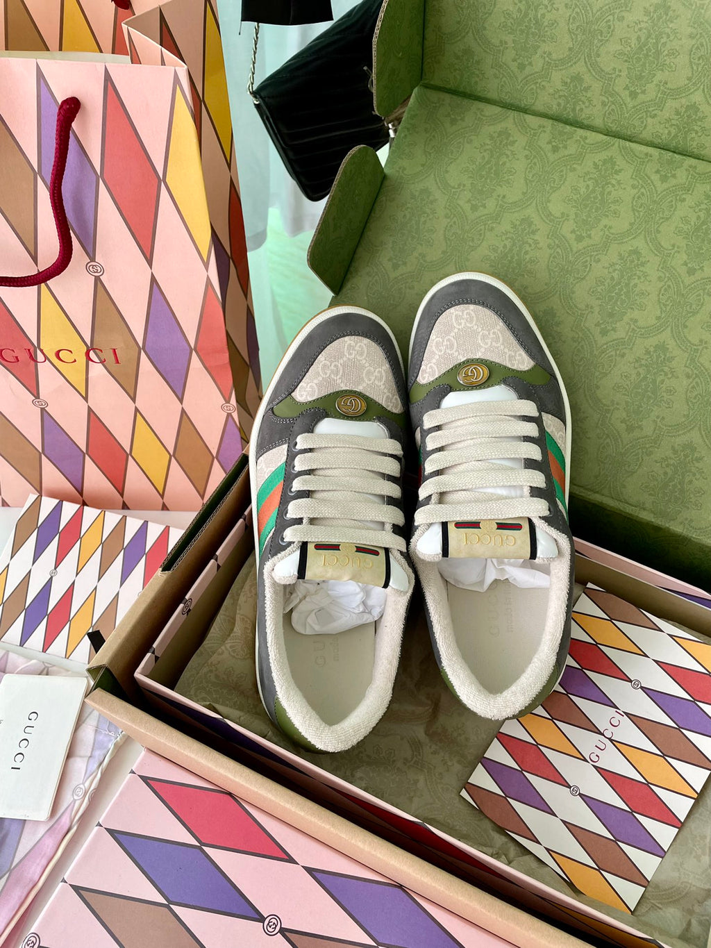 Gucci unisex sneakers laid in box with white laces, dark gray uppers, green/red stripe.