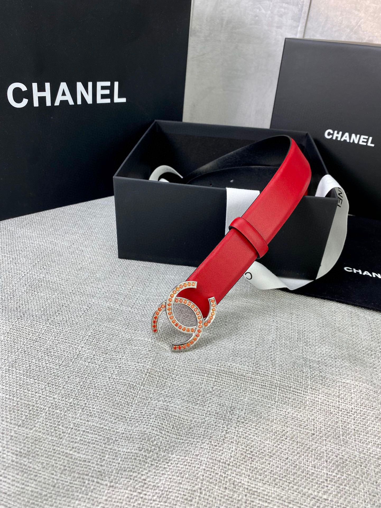 Red leather belt with gold-tone CC logo buckle resting in a gift box