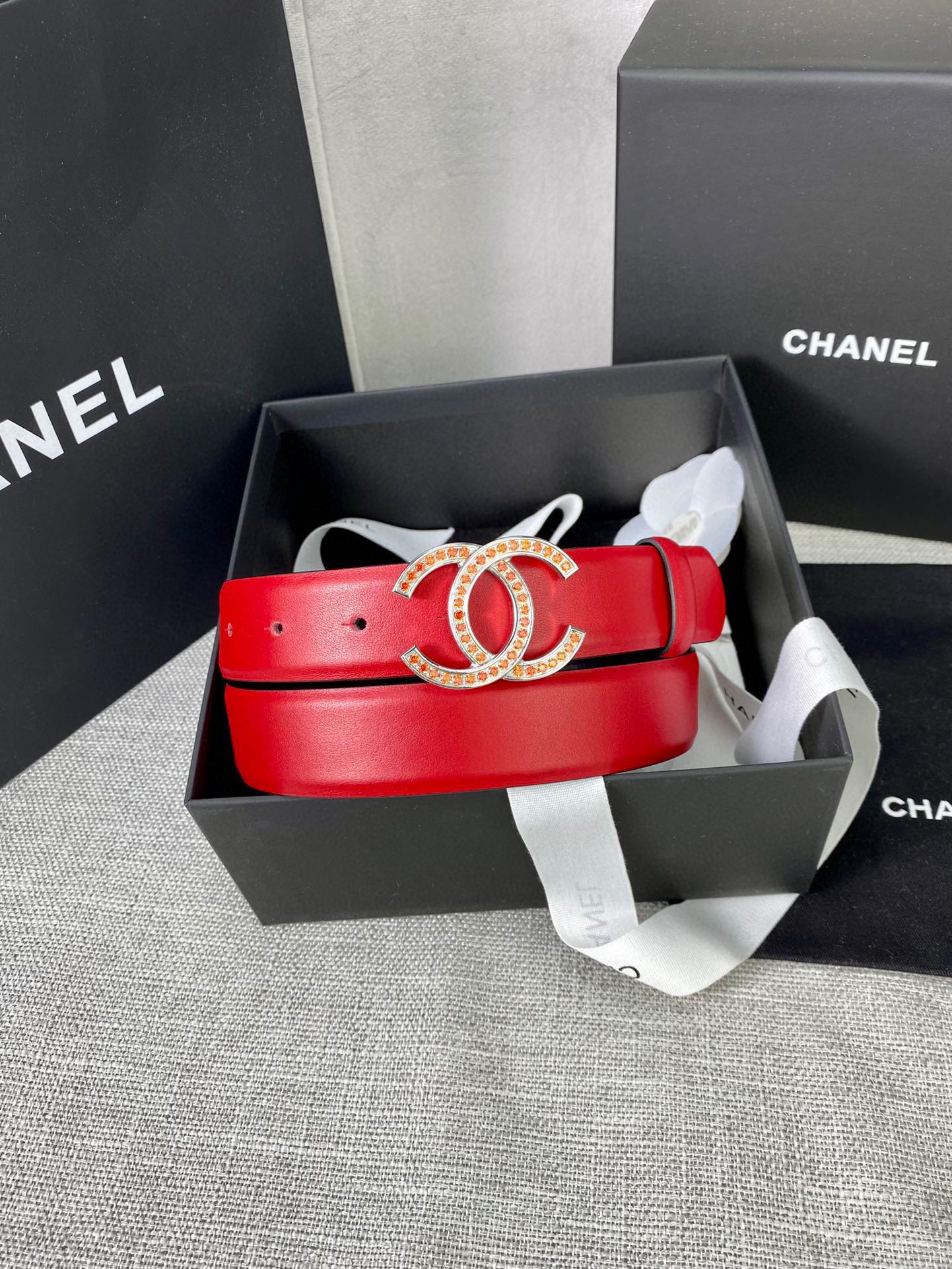 Red leather belt with gold-tone CC buckle in a box with ribbon and tissue