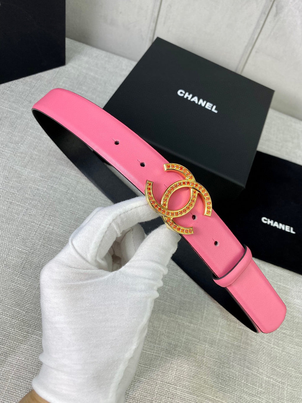 Pink leather belt with gold-tone CC buckle, held in a white glove