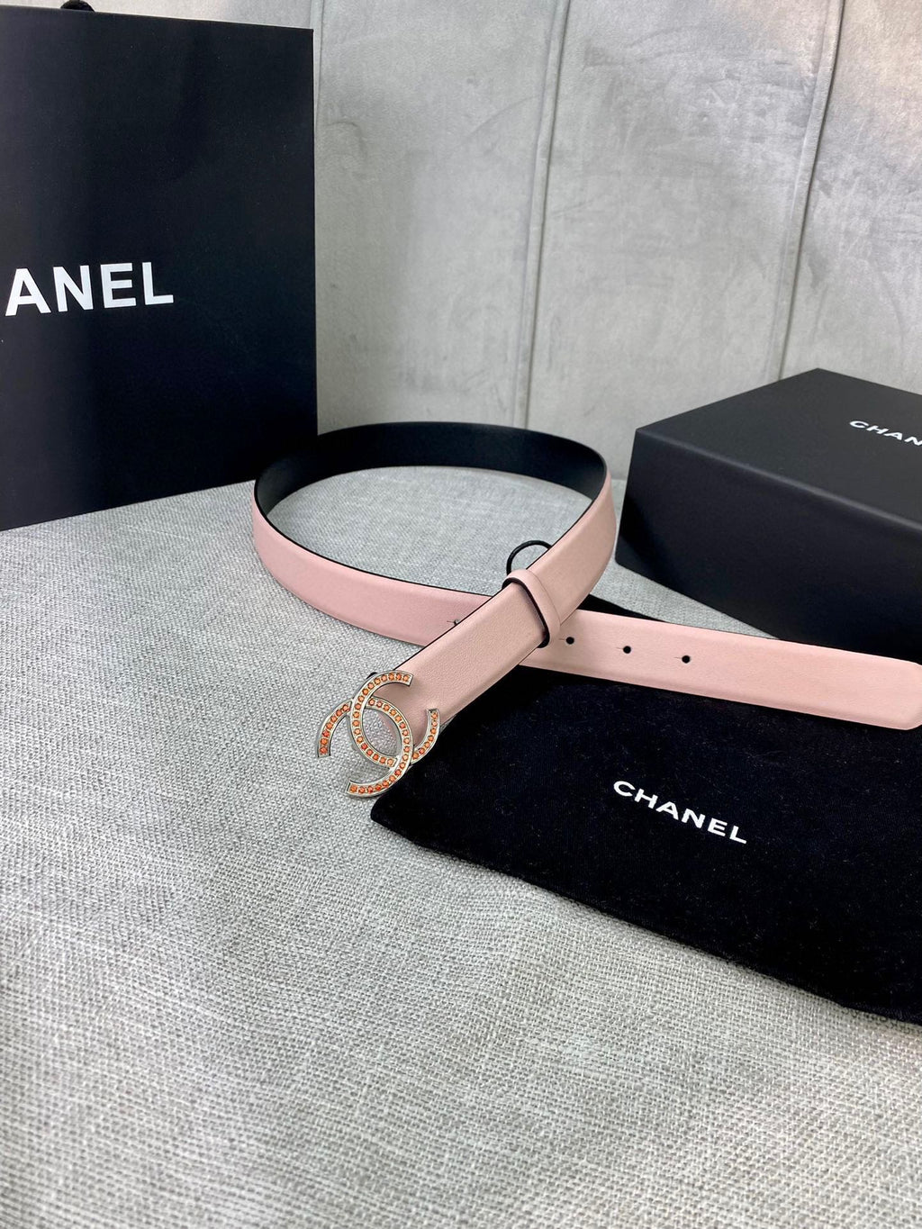 Light pink leather belt with gold logo buckle, coiled in front of gift box