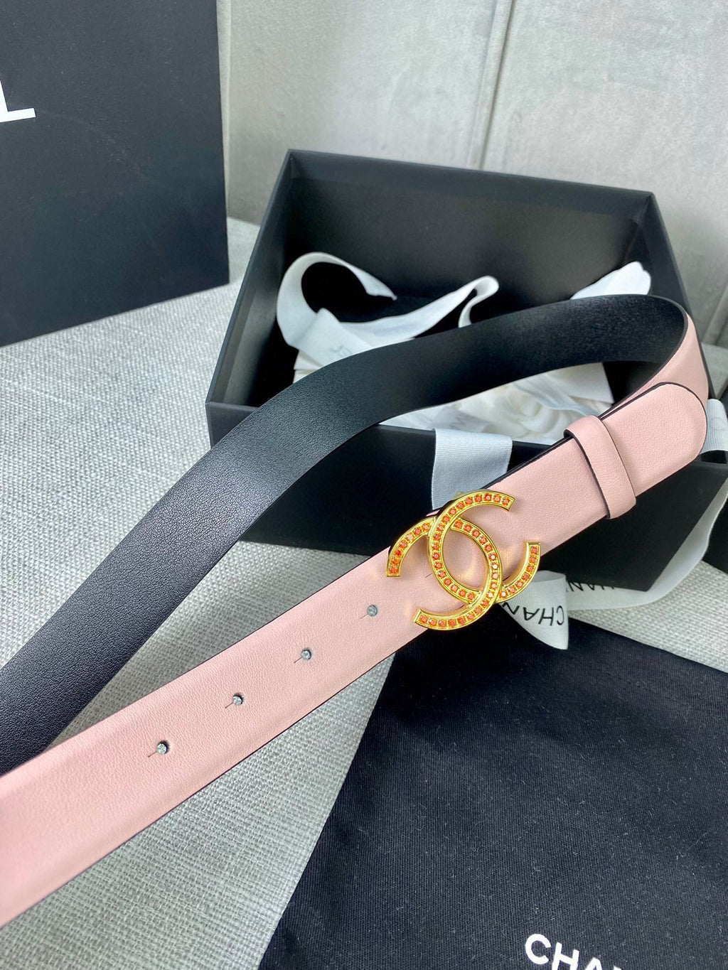 Light pink leather belt with gold logo buckle, laid across box with tissue