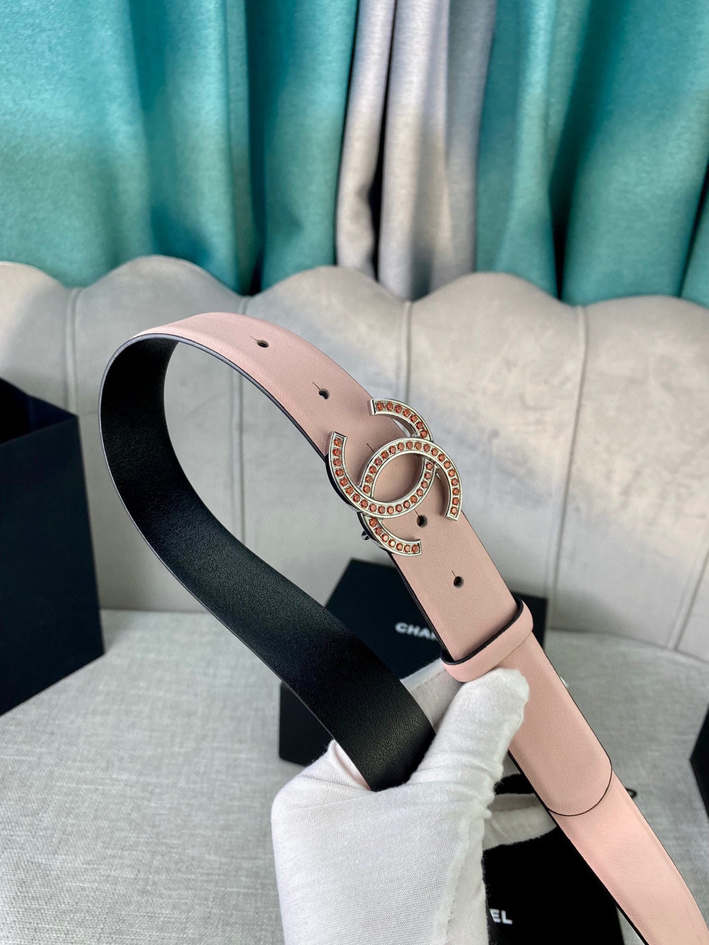 Light pink leather belt with gold logo buckle, angled view with white gloves