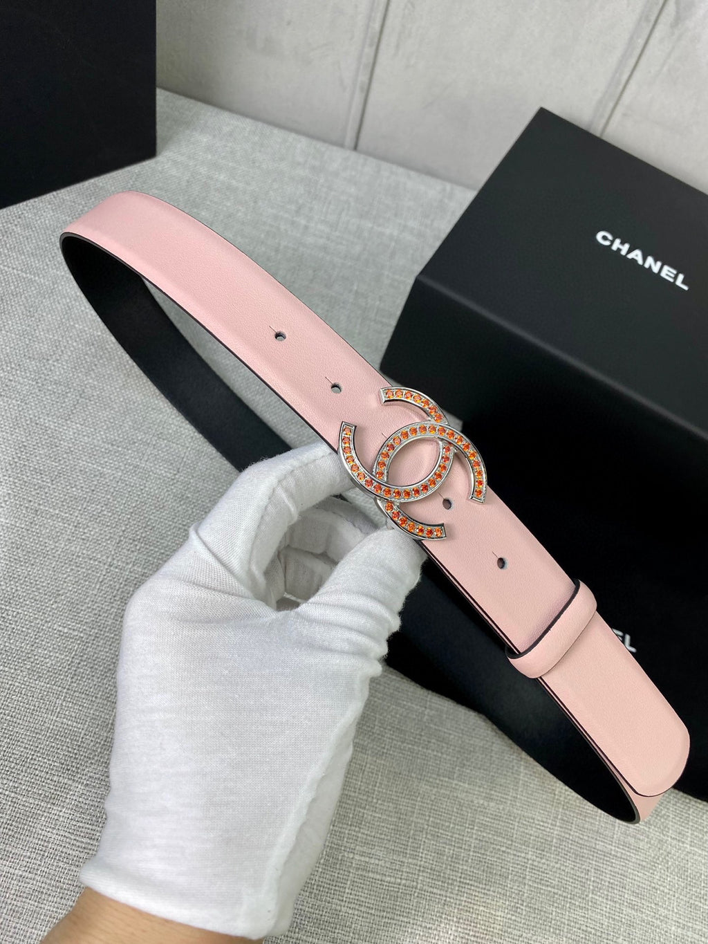 Light pink leather belt with gold logo buckle, front view on black box