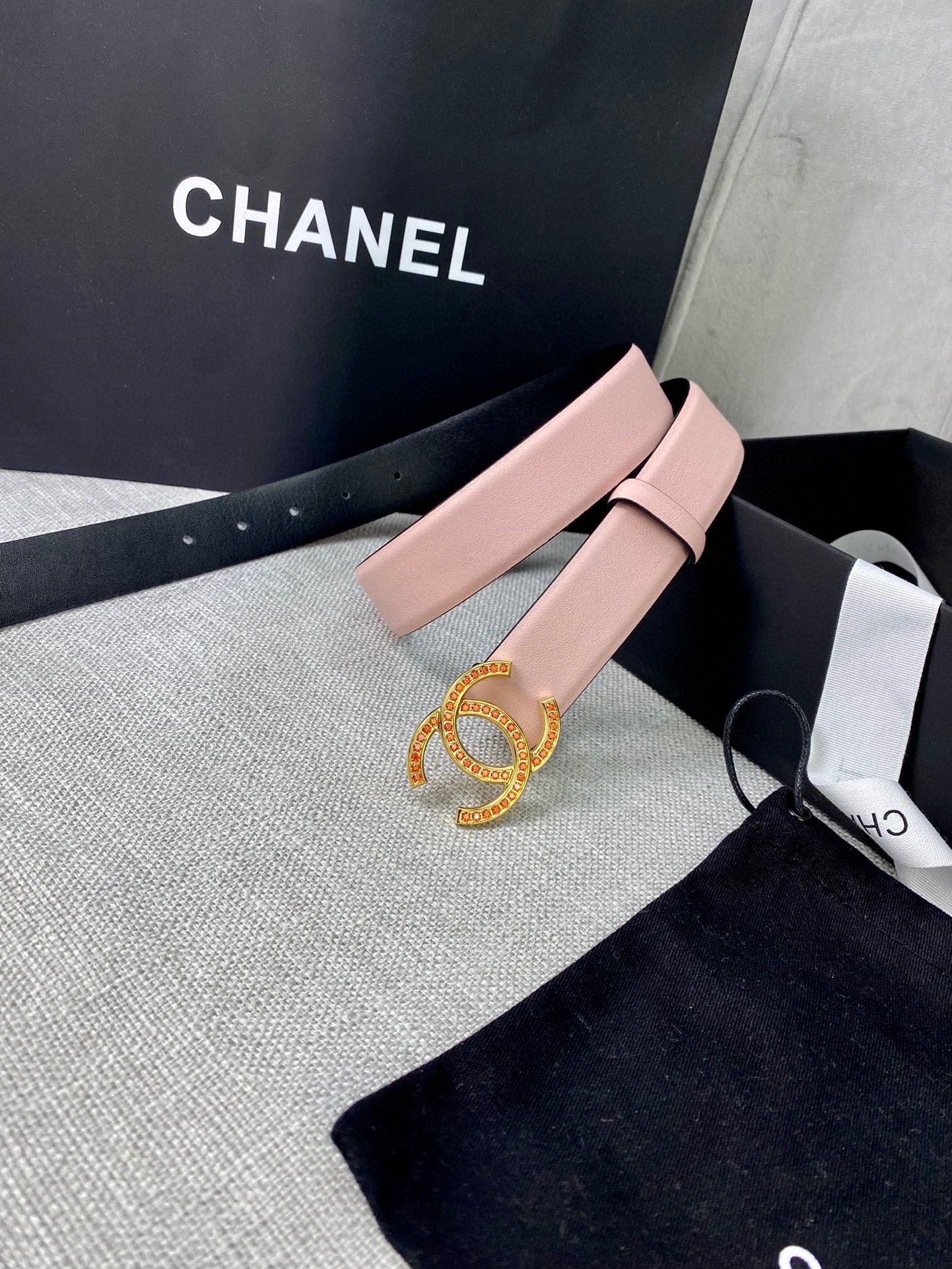 Light pink leather belt with ornate gold logo buckle, angled on display box