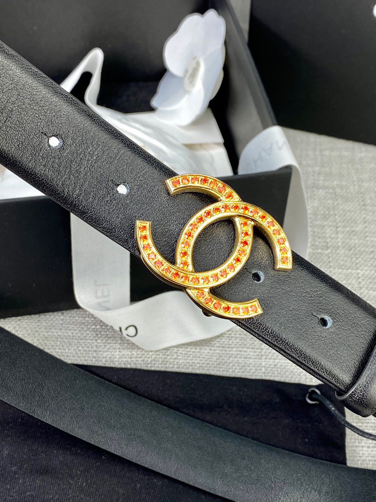 Black leather belt close-up: gold and red CC buckle on textured strap