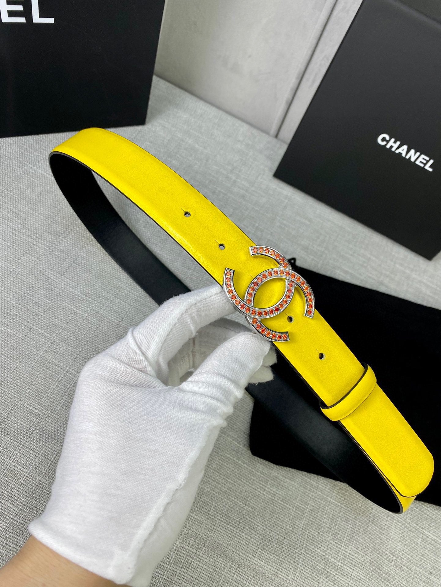 Yellow leather belt with gold-tone logo buckle, held near black inner lining