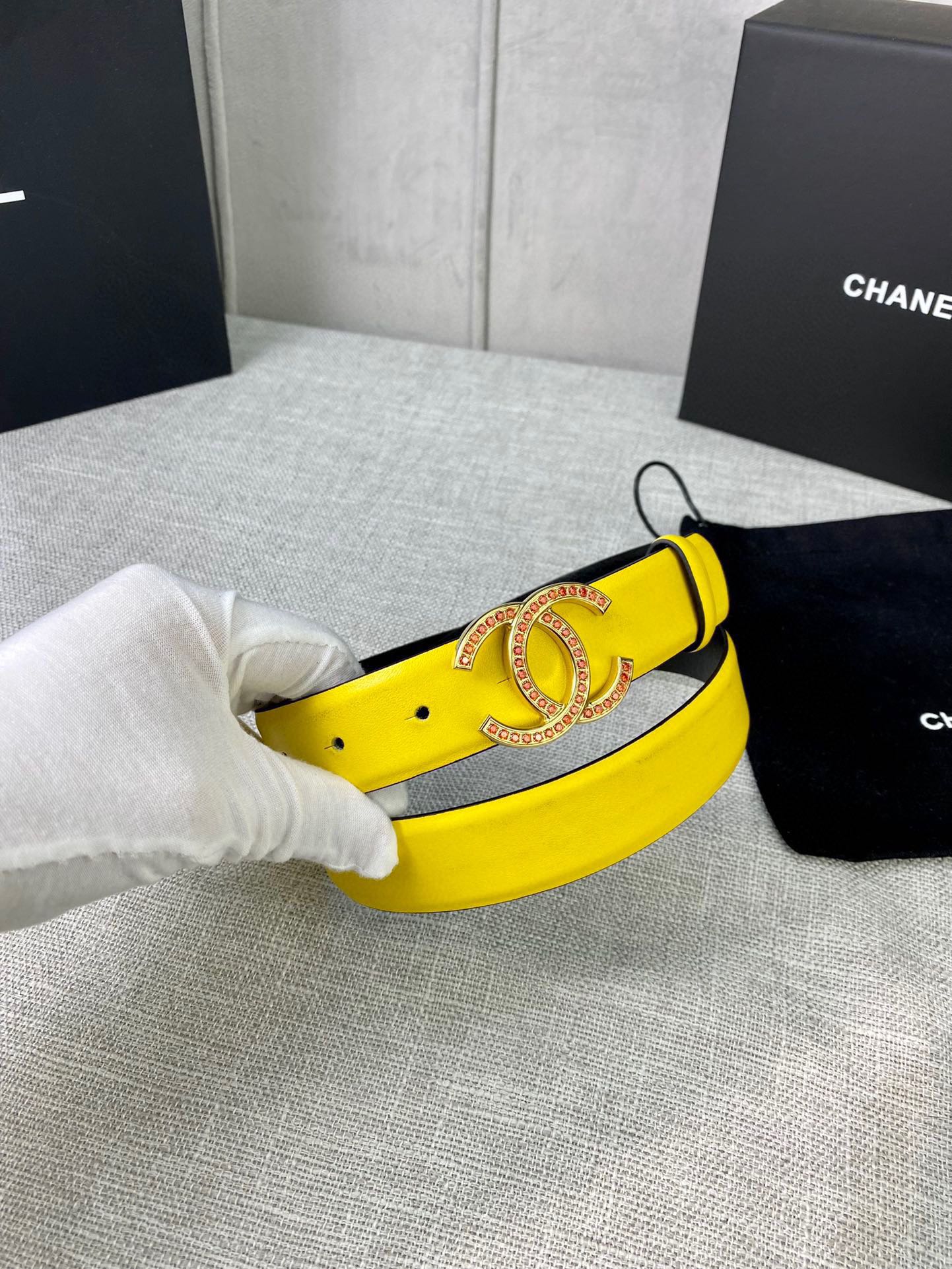 Yellow leather belt with ornate gold-tone logo buckle, held by white gloves