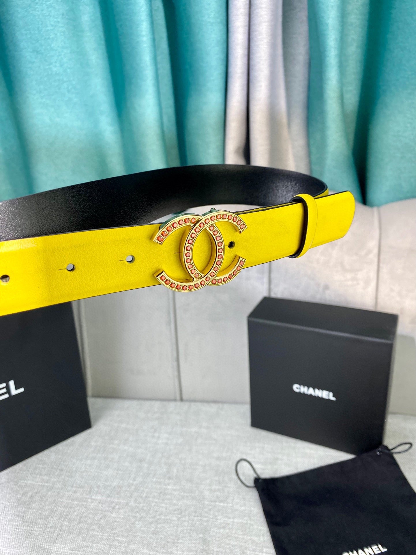 Yellow leather belt with gold-tone logo buckle, resting beside a black pouch