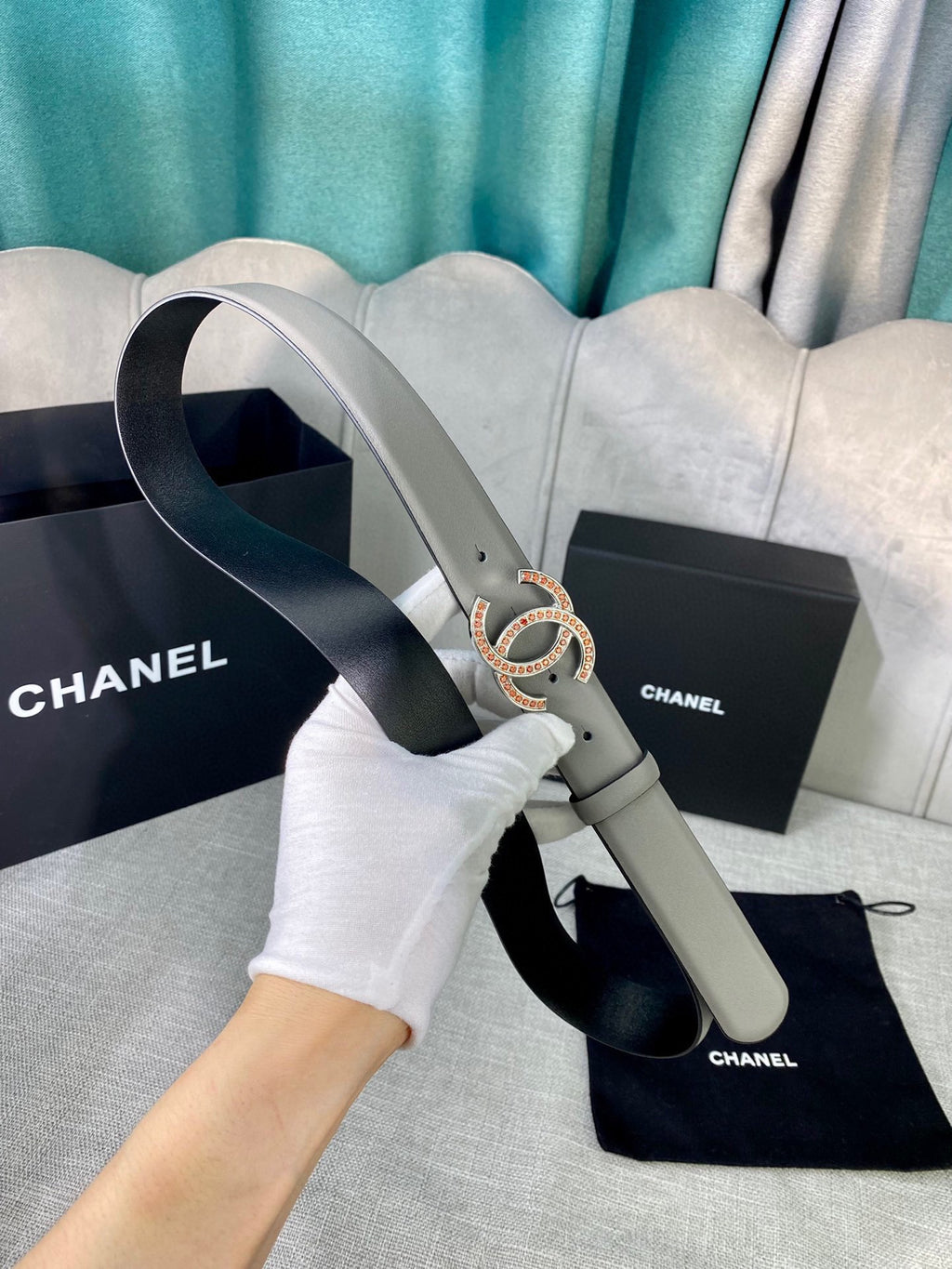 Light gray belt with oval CC buckle, shown with gloved hand and pouch