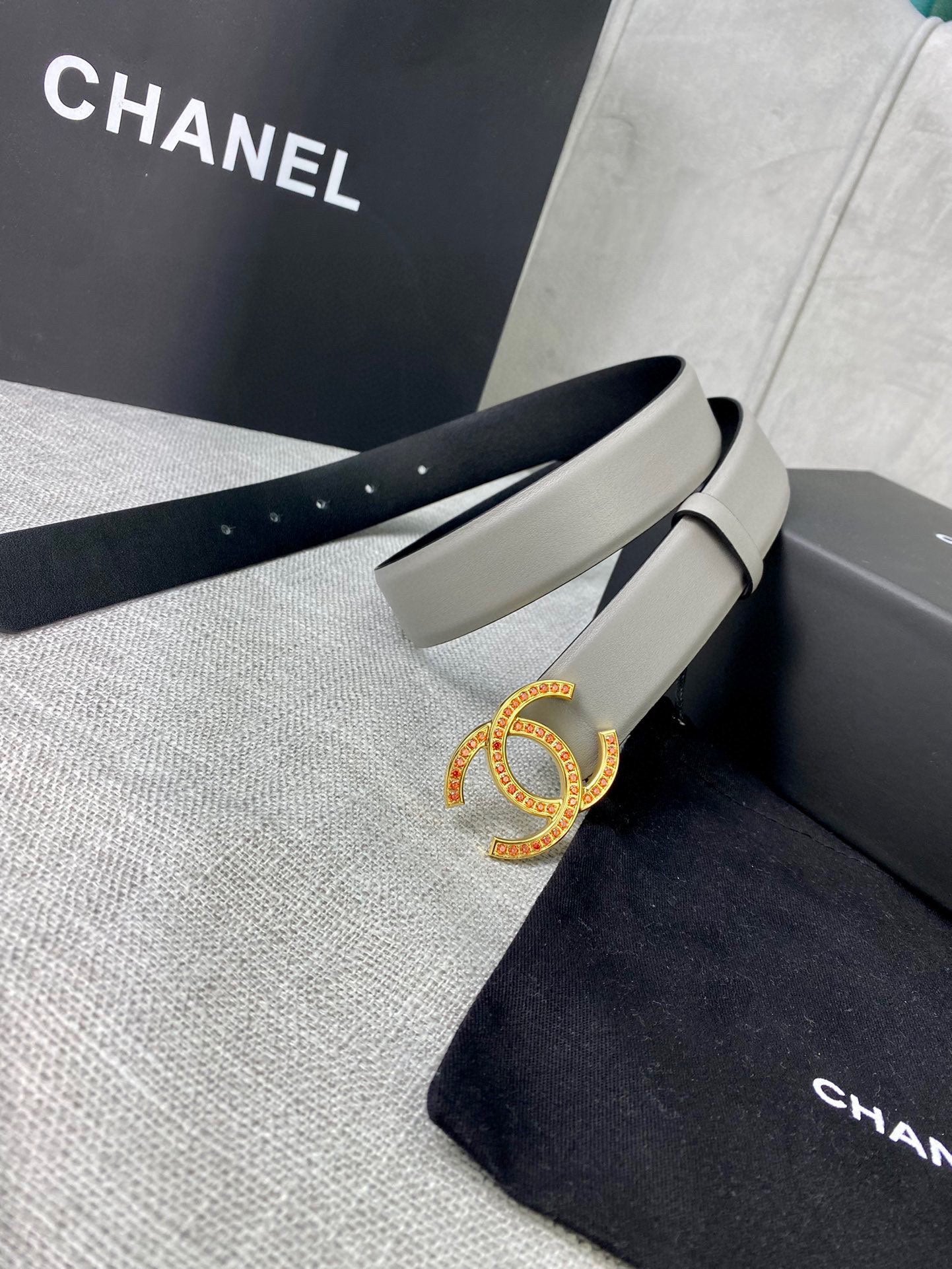 Light gray belt with oval CC buckle, laid over Chanel dust bag