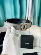 Light gray leather belt with oval CC buckle, close-up with box and bag
