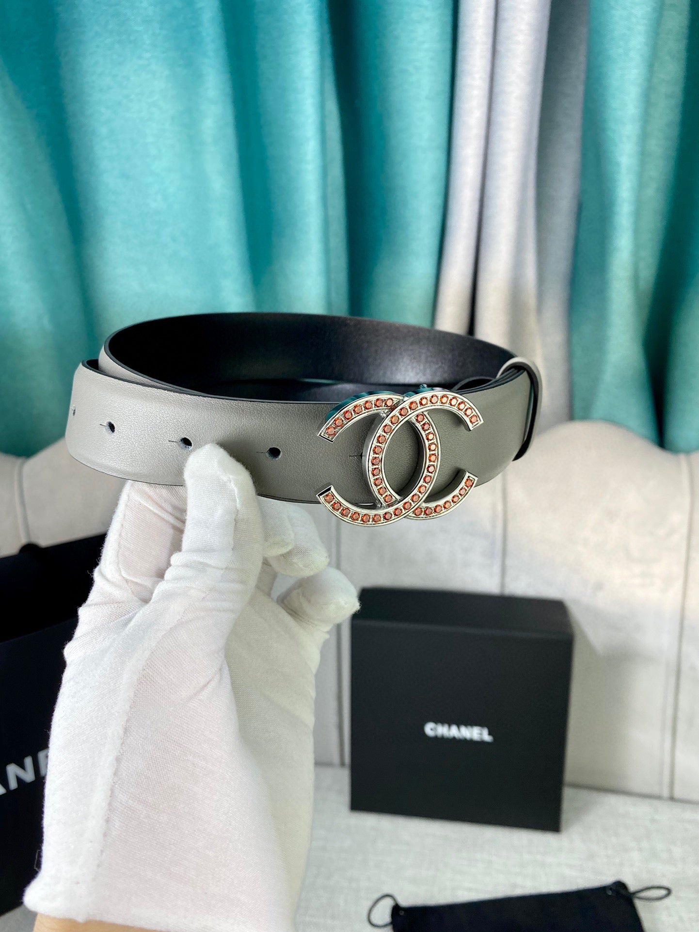 Light gray leather belt with oval CC buckle, close-up with box and bag