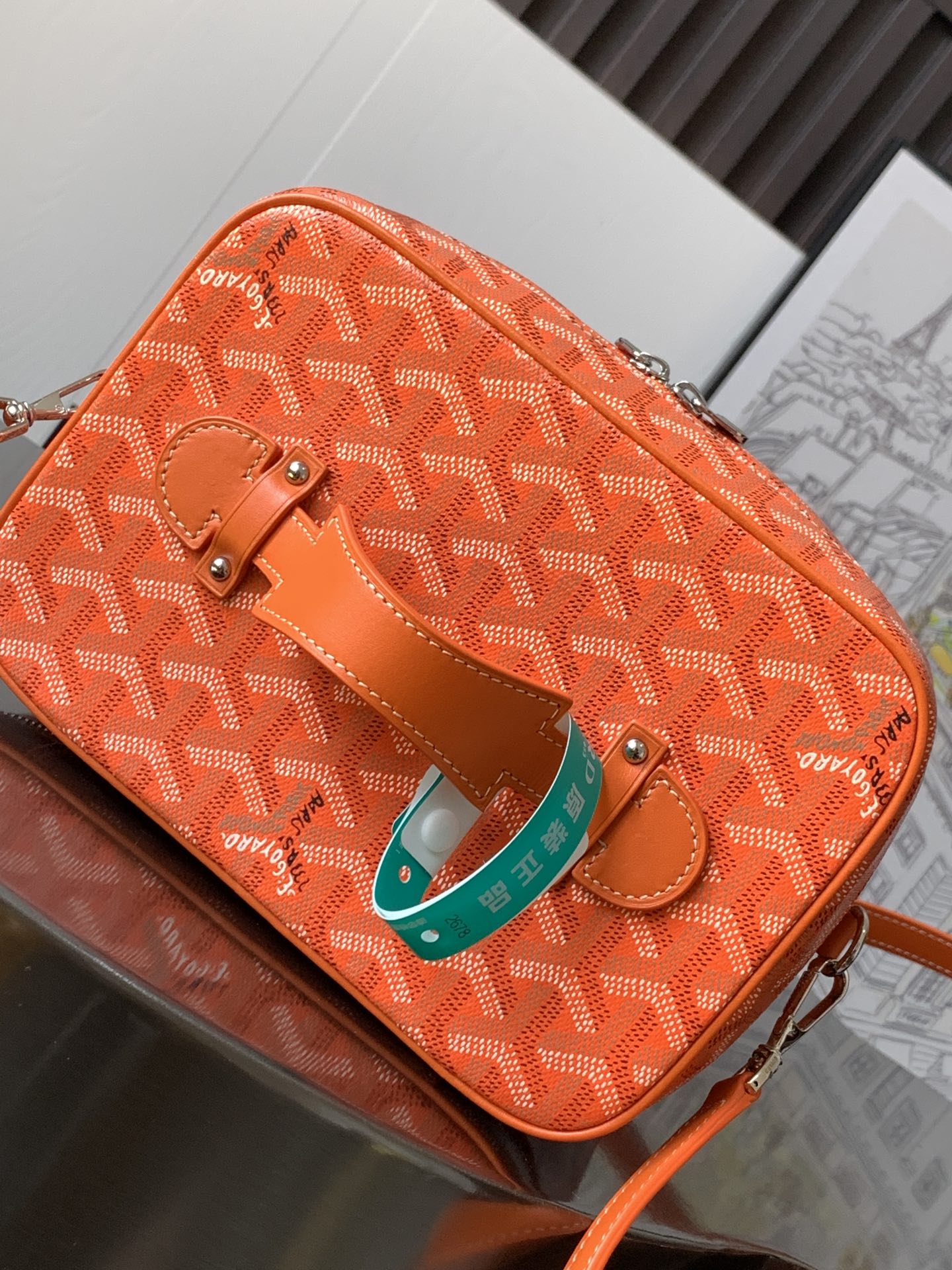 Small orange patterned bag with flap, shoulder strap, and turquoise hanging tag