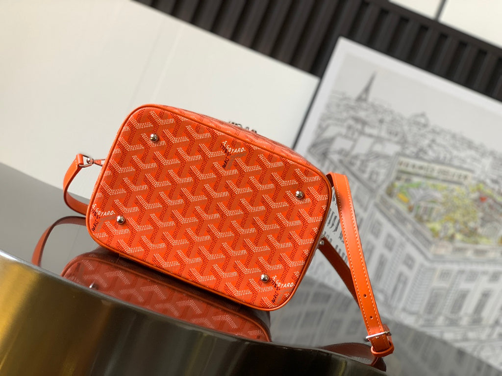 Goyard bag in bright orange with monogram pattern, studded details, and crossbody strap