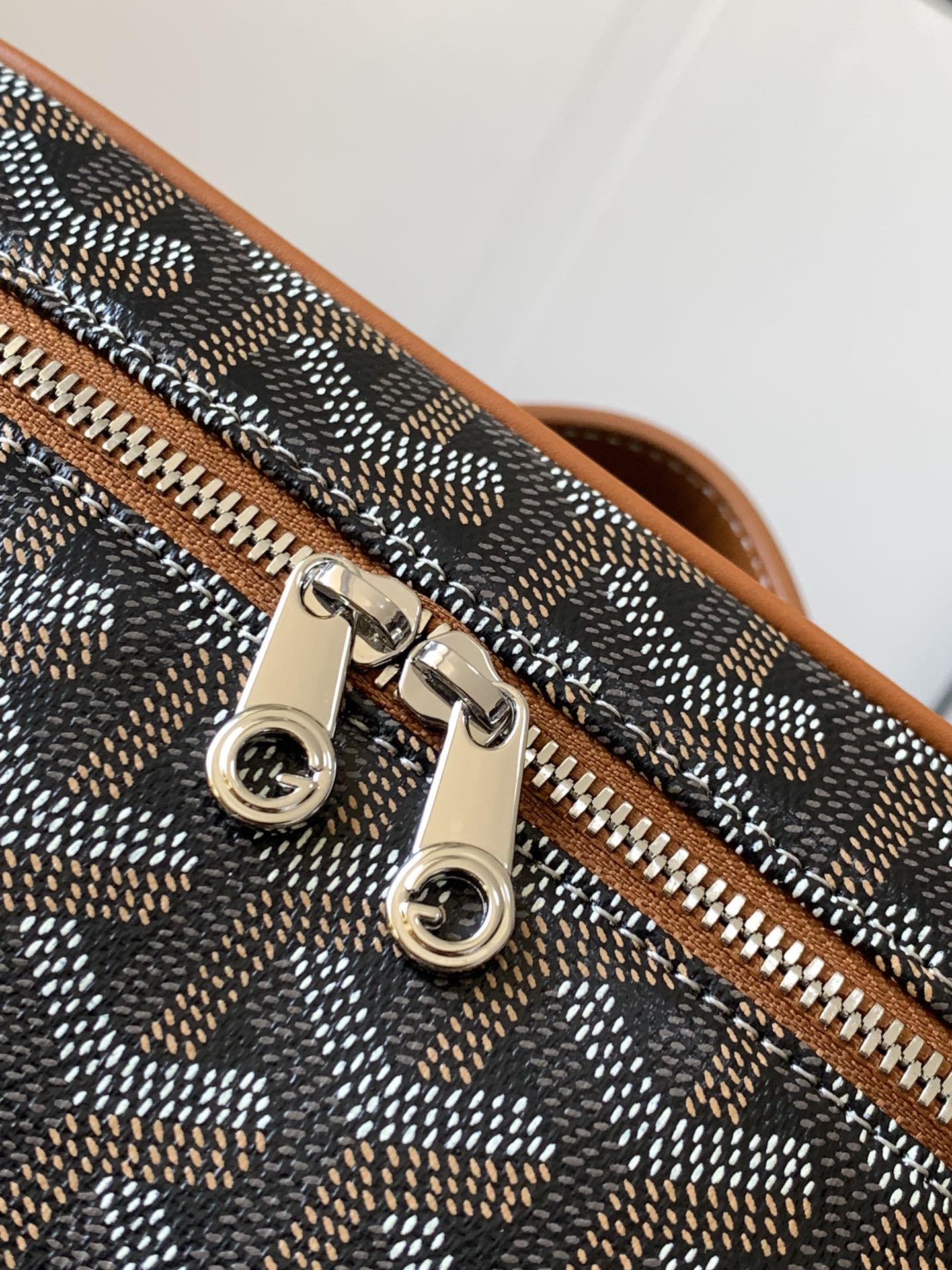 Small crossbody bag detail: silver-tone zipper pulls and metal rings on tan trim.