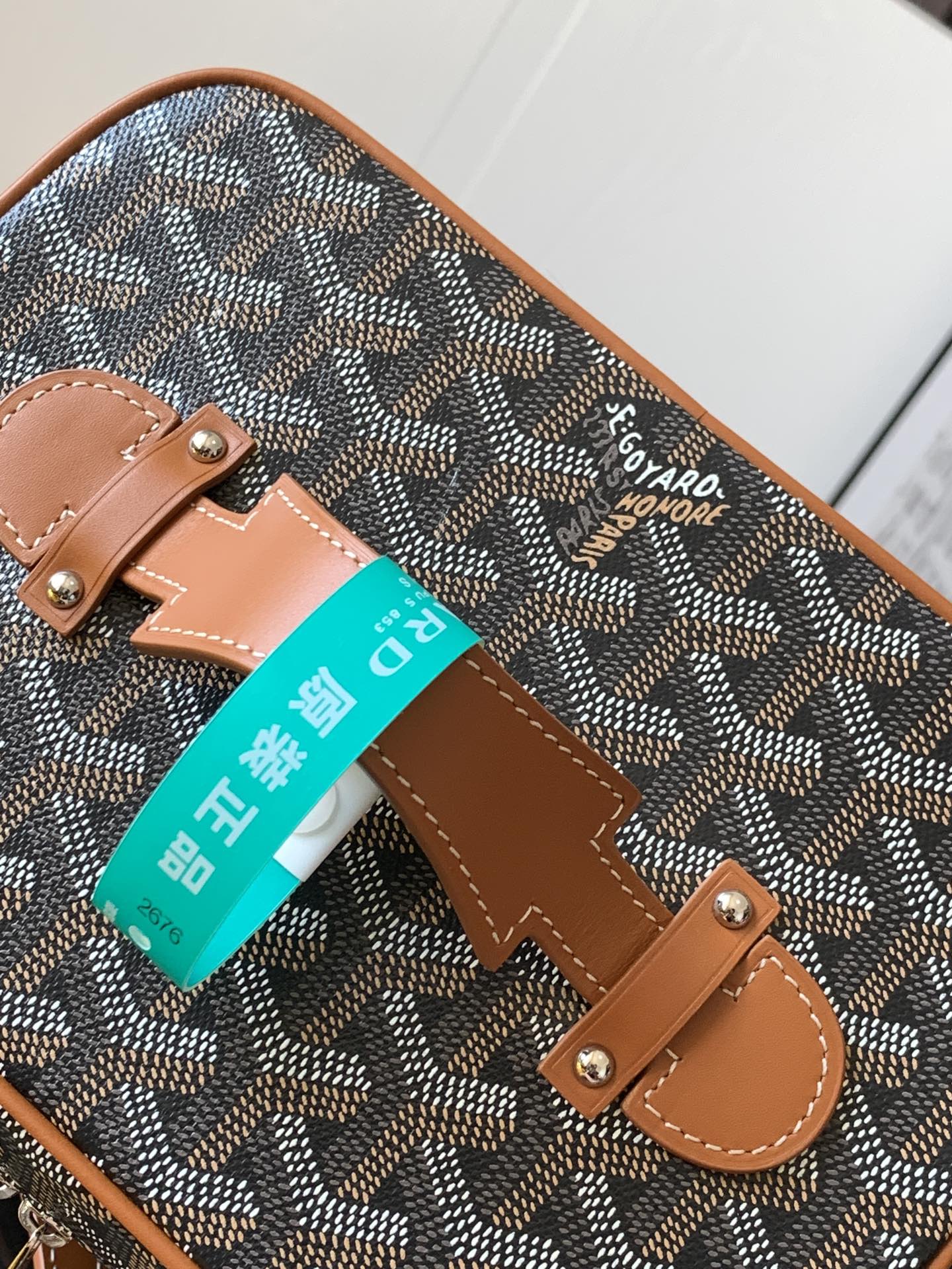 Small crossbody bag detail: tan handle strap, brown leather patch, teal tag attached.