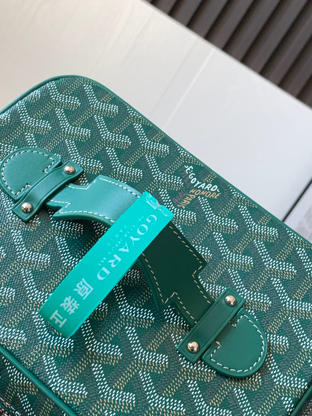 Goyard teal bag detail with leather corner tab, front strap loop, and brand tag