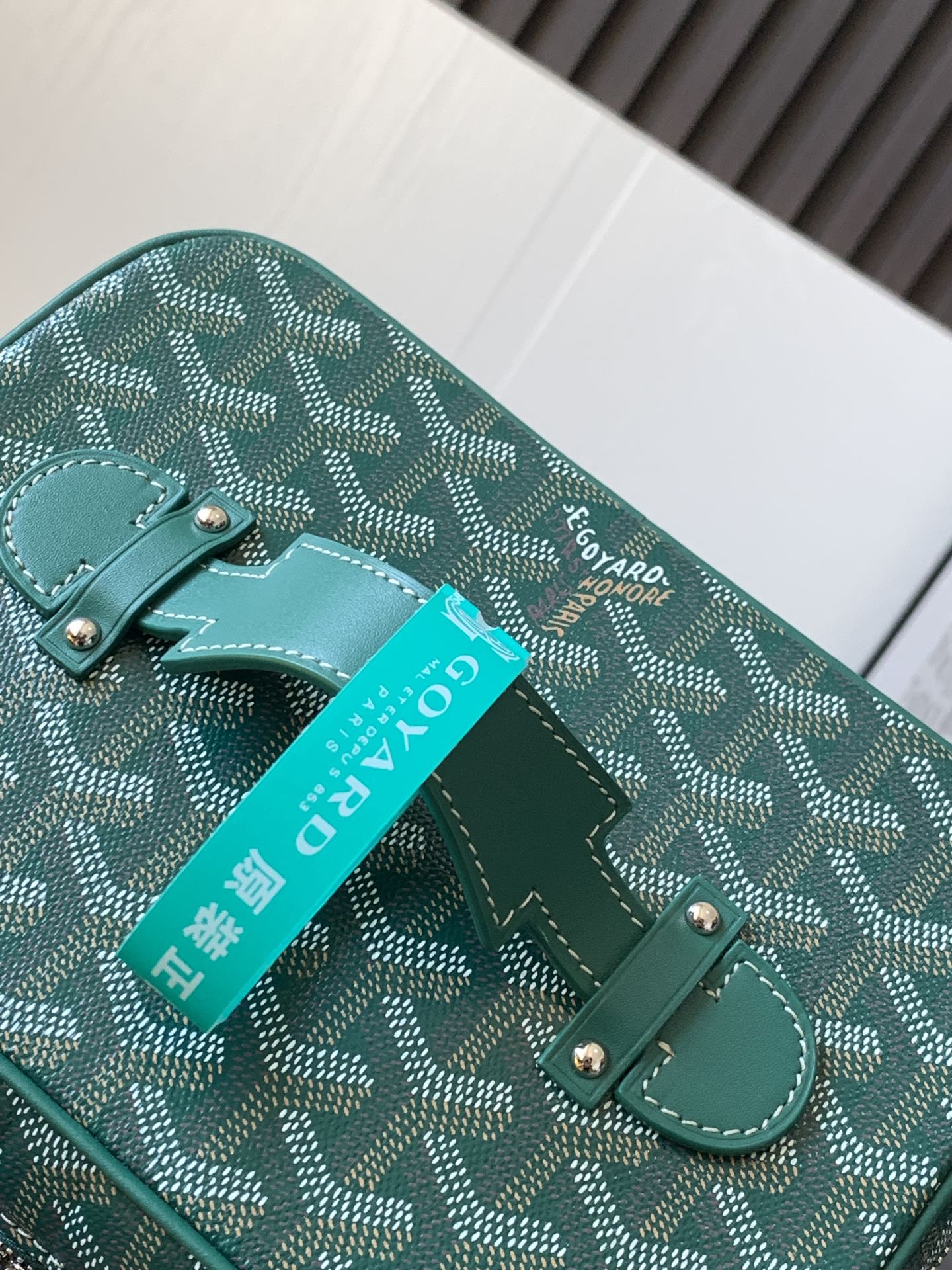 Goyard teal bag detail with leather corner tab, front strap loop, and brand tag
