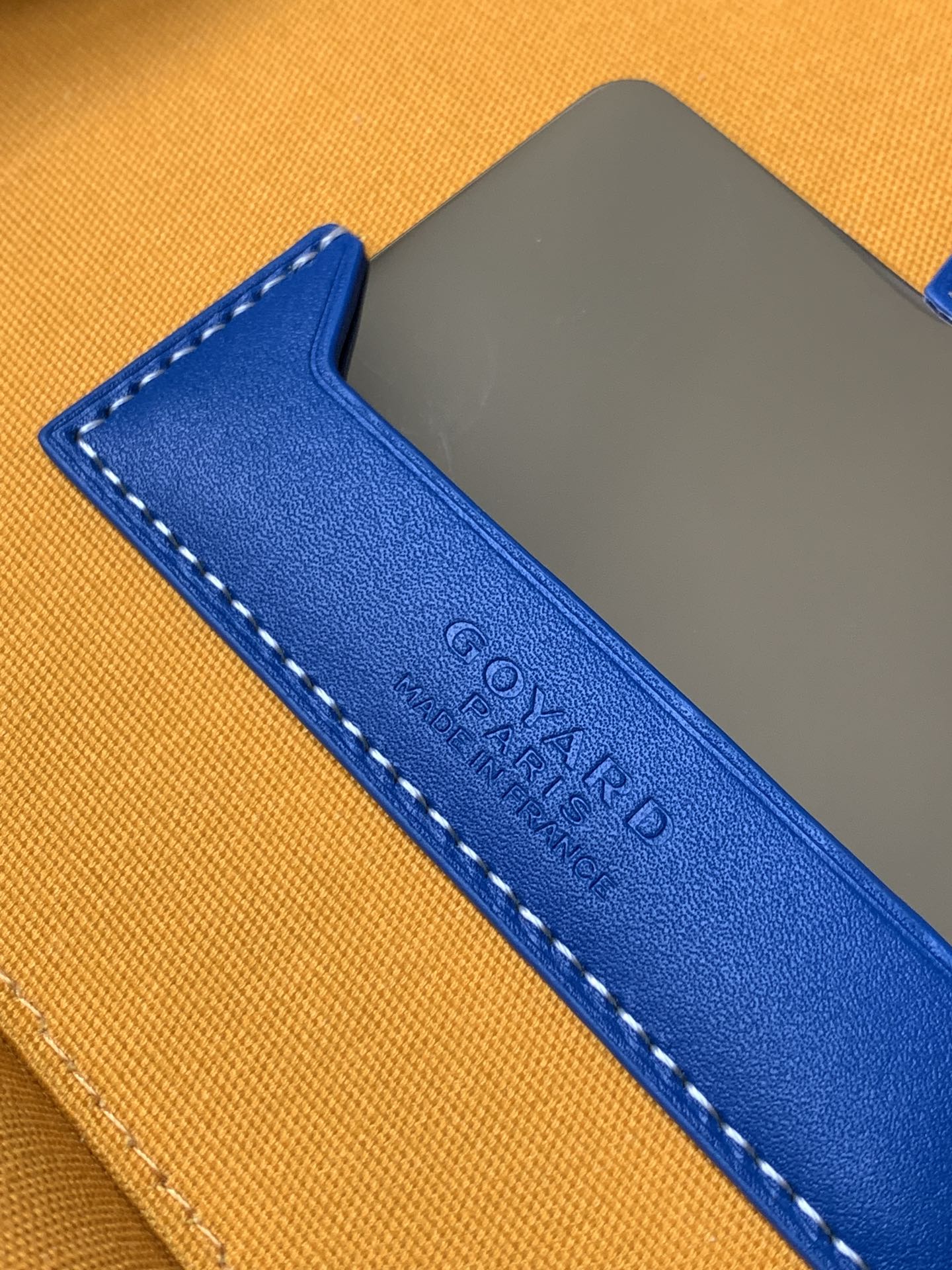 Blue leather strap patch with stamped lettering on an orange bag panel